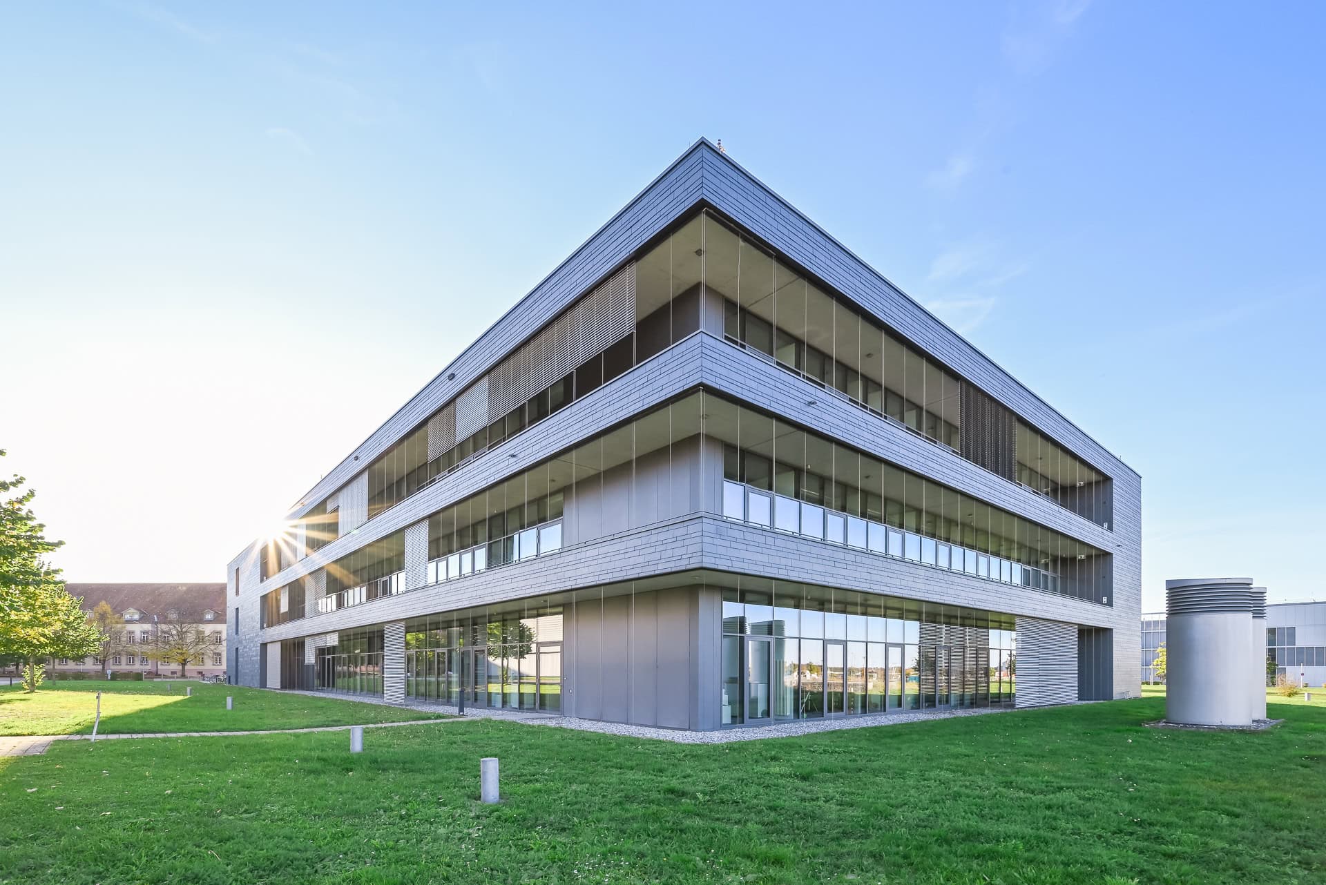 Außenansicht von FIT Materialforschung Freiburg mit grauer Fassade, Glasflächen und Sonnenstern. Architektur von ArGe Architekten, Leins | Ohnemus, Freie Architekten | Part mbB. Foto: Bertrand Weiss, weissfotografie.com.