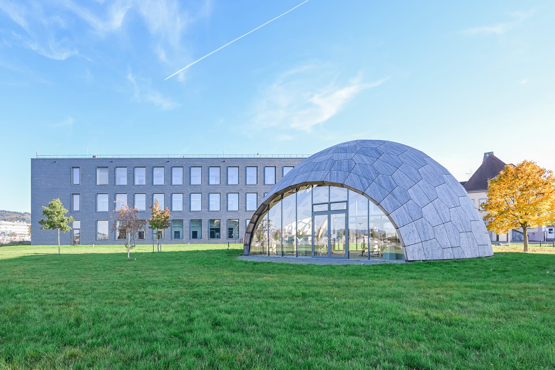 Kuppelförmiger Holzkörper von FIT Materialforschung Freiburg vor dem linearen Forschungsgebäude. Architektur von ArGe Architekten, Leins | Ohnemus, Freie Architekten | Part mbB. Foto: Bertrand Weiss, weissfotografie.com.