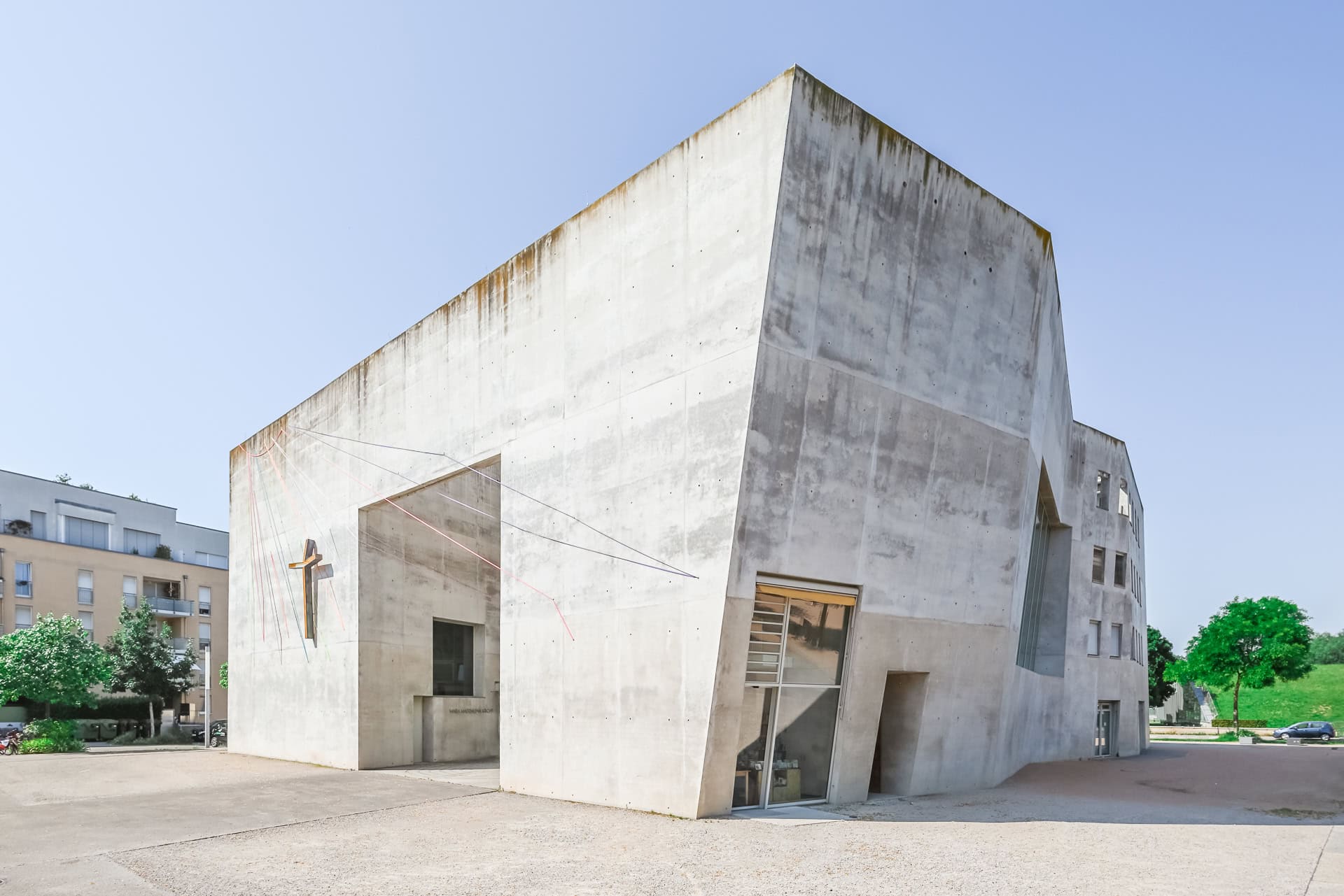 Außenansicht der Maria-Magdalena-Kirche mit Kreuz, schrägen Betonflächen und großem Fassadeneinschnitt. Architektur von Kister Scheithauer Gross. Foto: Bertrand Weiss, weissfotografie.com.