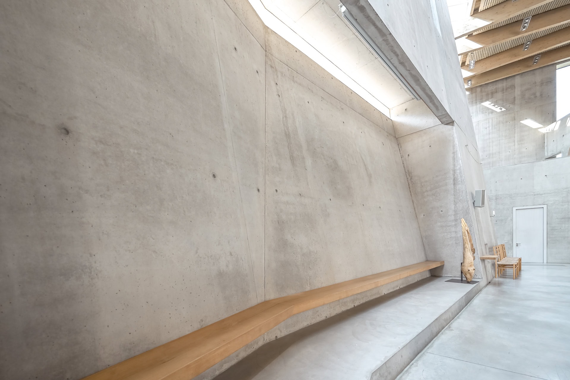 Innenraum der Maria-Magdalena-Kirche mit Sichtbetonwand und langer Holzbank. Architektur von Kister Scheithauer Gross. Foto: Bertrand Weiss, weissfotografie.com.