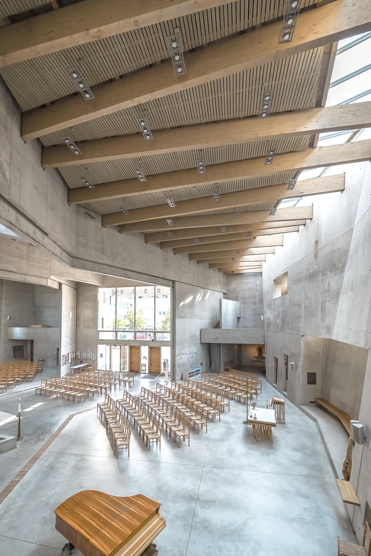Blick von oben in den hohen Kirchenraum mit Holzdach, Sichtbeton und geordneten Stuhlreihen. Architektur von Kister Scheithauer Gross. Foto: Bertrand Weiss, weissfotografie.com.