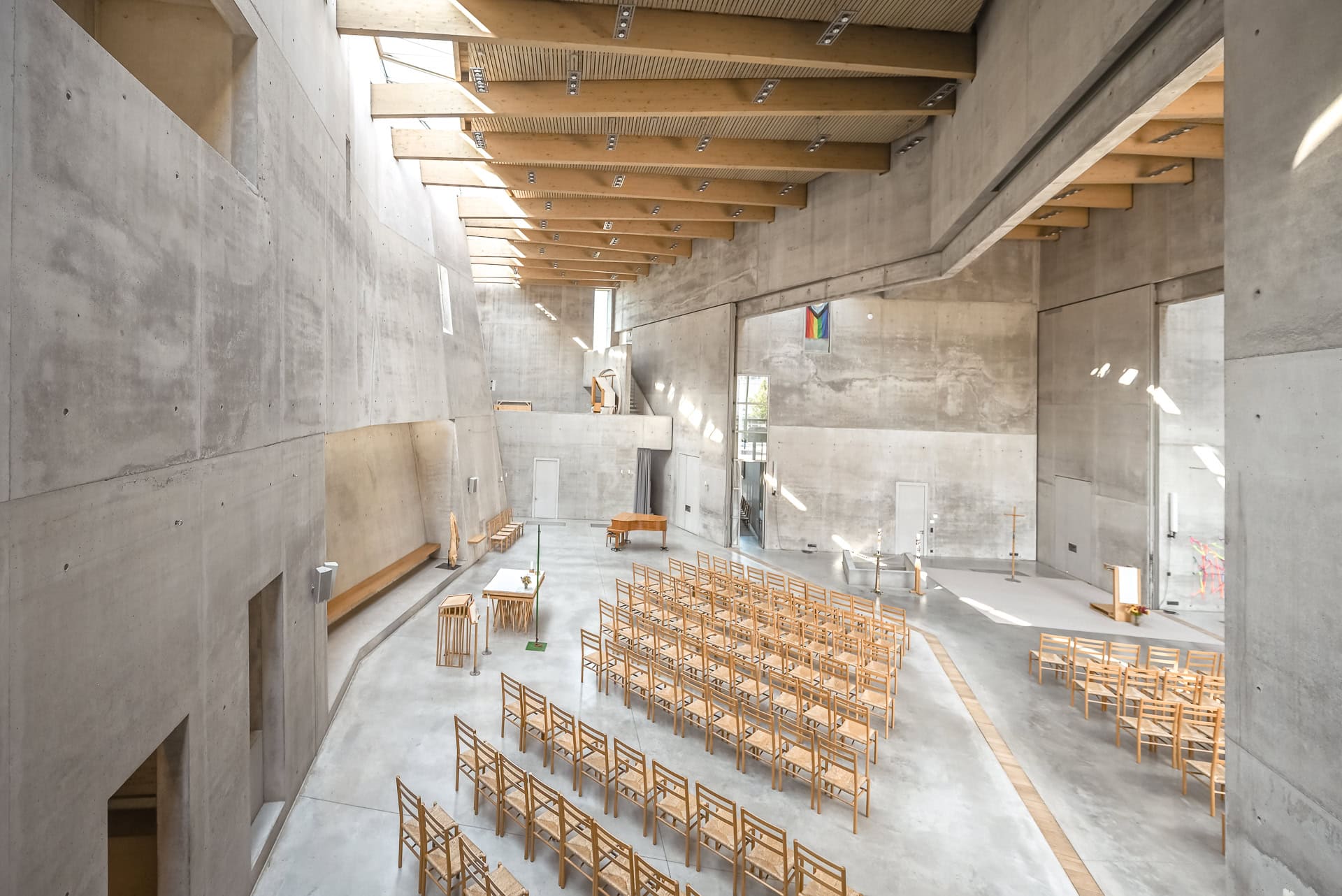 Erhöhter Blick in den Kirchenraum mit Betonwänden, Holzdecke und einfallendem Tageslicht. Architektur von Kister Scheithauer Gross. Foto: Bertrand Weiss, weissfotografie.com.