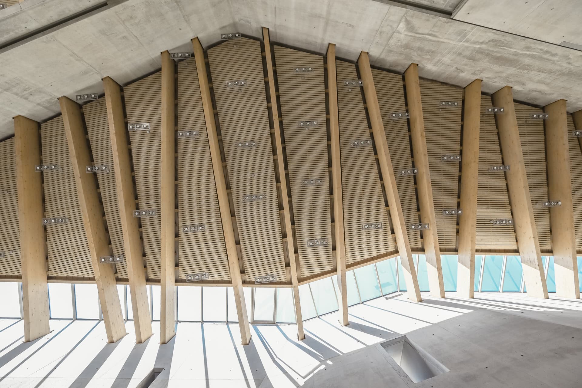 Holzdachkonstruktion der Maria-Magdalena-Kirche mit Lichtbändern und Schatten auf Betonflächen. Architektur von Kister Scheithauer Gross. Foto: Bertrand Weiss, weissfotografie.com.