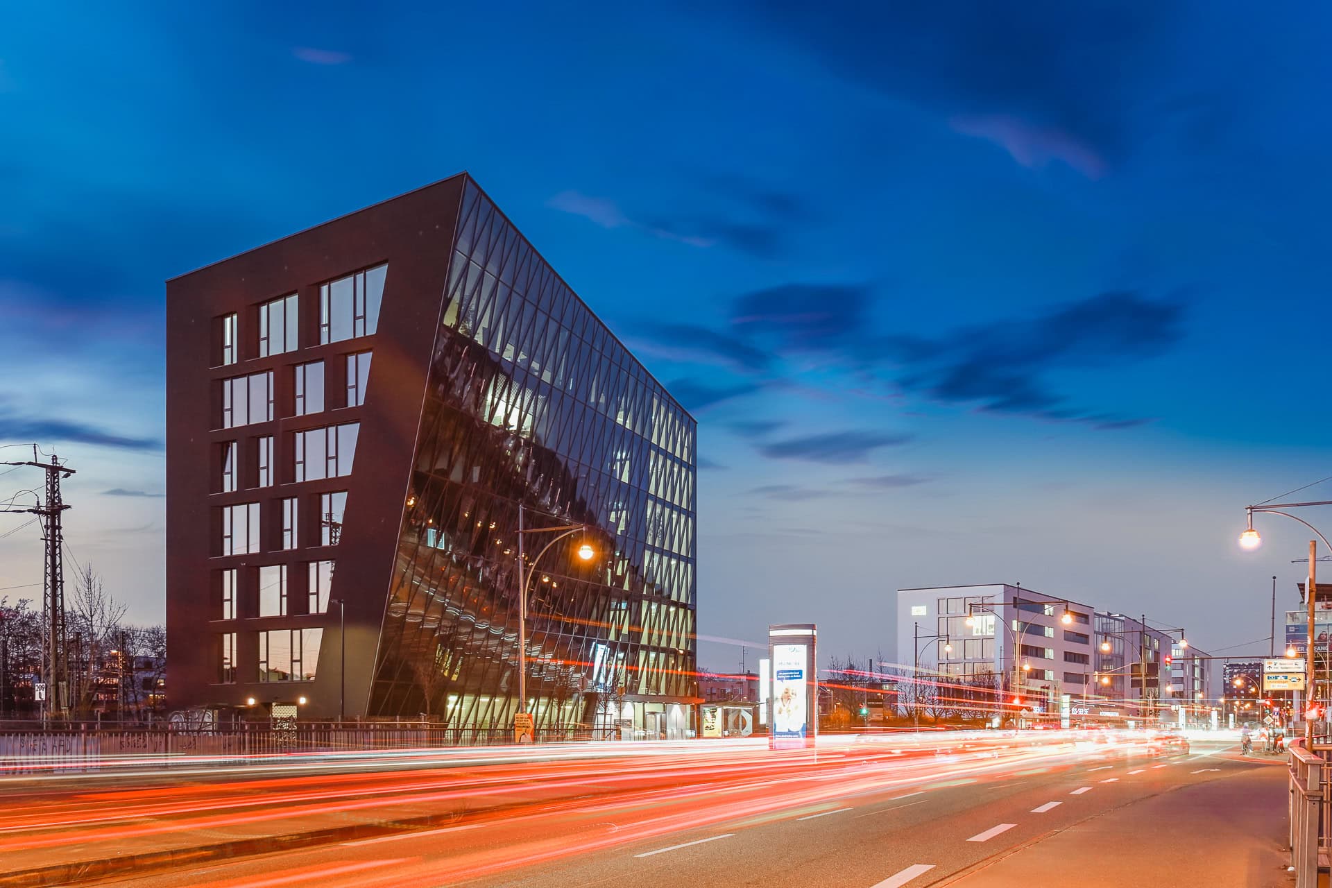 Schnewlin 12 Freiburg in der Blauen Stunde mit geneigter Glasfassade und Lichtspuren im Straßenraum. Architektur von hotz+architekten. Foto: Bertrand Weiss, weissfotografie.com.