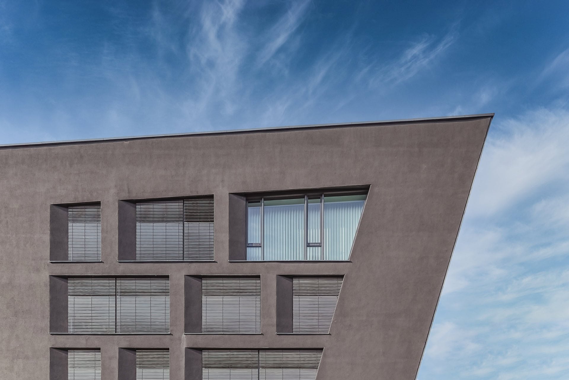 Fassadendetail von Schnewlin 12 Freiburg mit dunkler Putzfläche, Fenstern und schräger Gebäudekante. Architektur von hotz+architekten. Foto: Bertrand Weiss, weissfotografie.com.