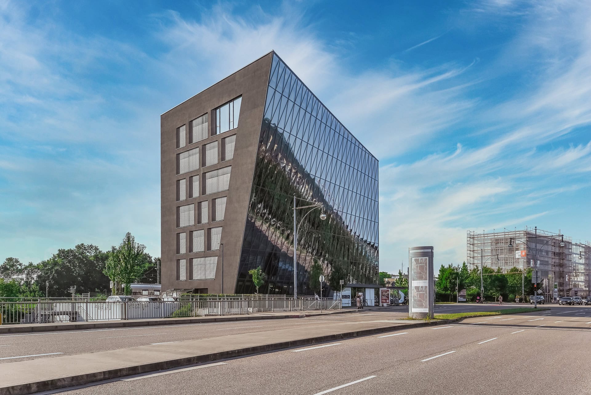Gesamtansicht von Schnewlin 12 Freiburg an der Straße mit spiegelnder Glasfassade und Stadtraum. Architektur von hotz+architekten. Foto: Bertrand Weiss, weissfotografie.com.