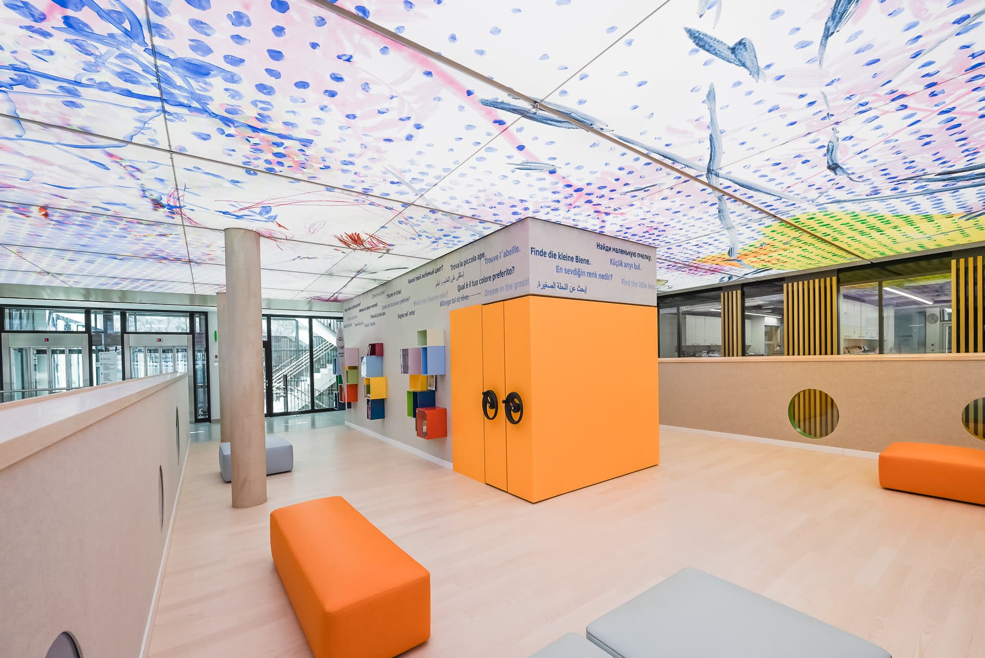 Innenbereich der Kinder- und Jugendklinik Freiburg mit farbiger Decke, Spielwand und orangefarbenen Sitzmodulen. Architektur von Heinle, Wischer und Partner. Foto: Bertrand Weiss, weissfotografie.com.