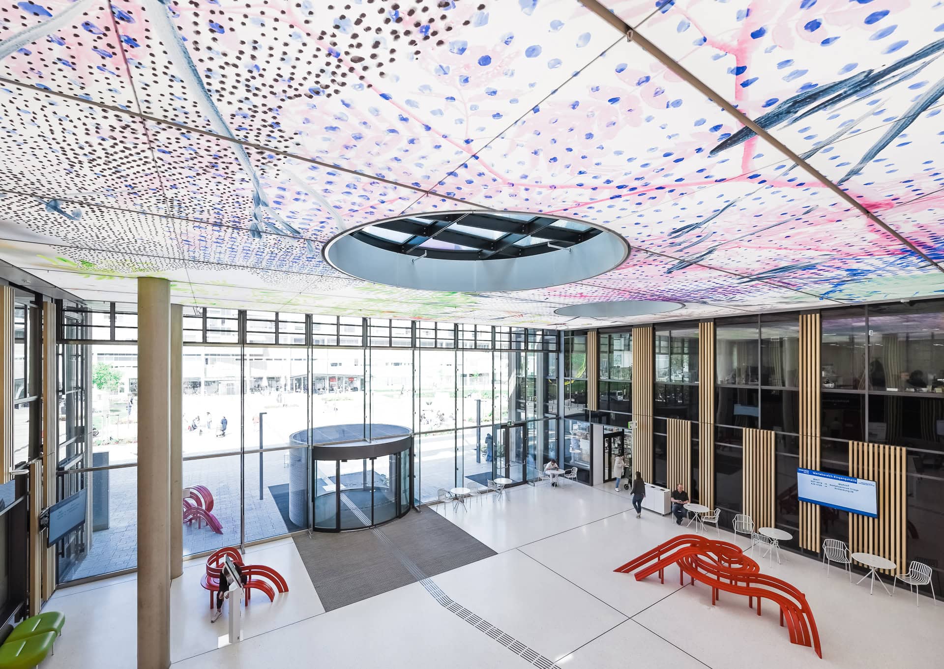 Eingangshalle der Kinder- und Jugendklinik Freiburg mit bemalter Decke, Glasfassade und roten Sitzobjekten. Architektur von Heinle, Wischer und Partner. Foto: Bertrand Weiss, weissfotografie.com.