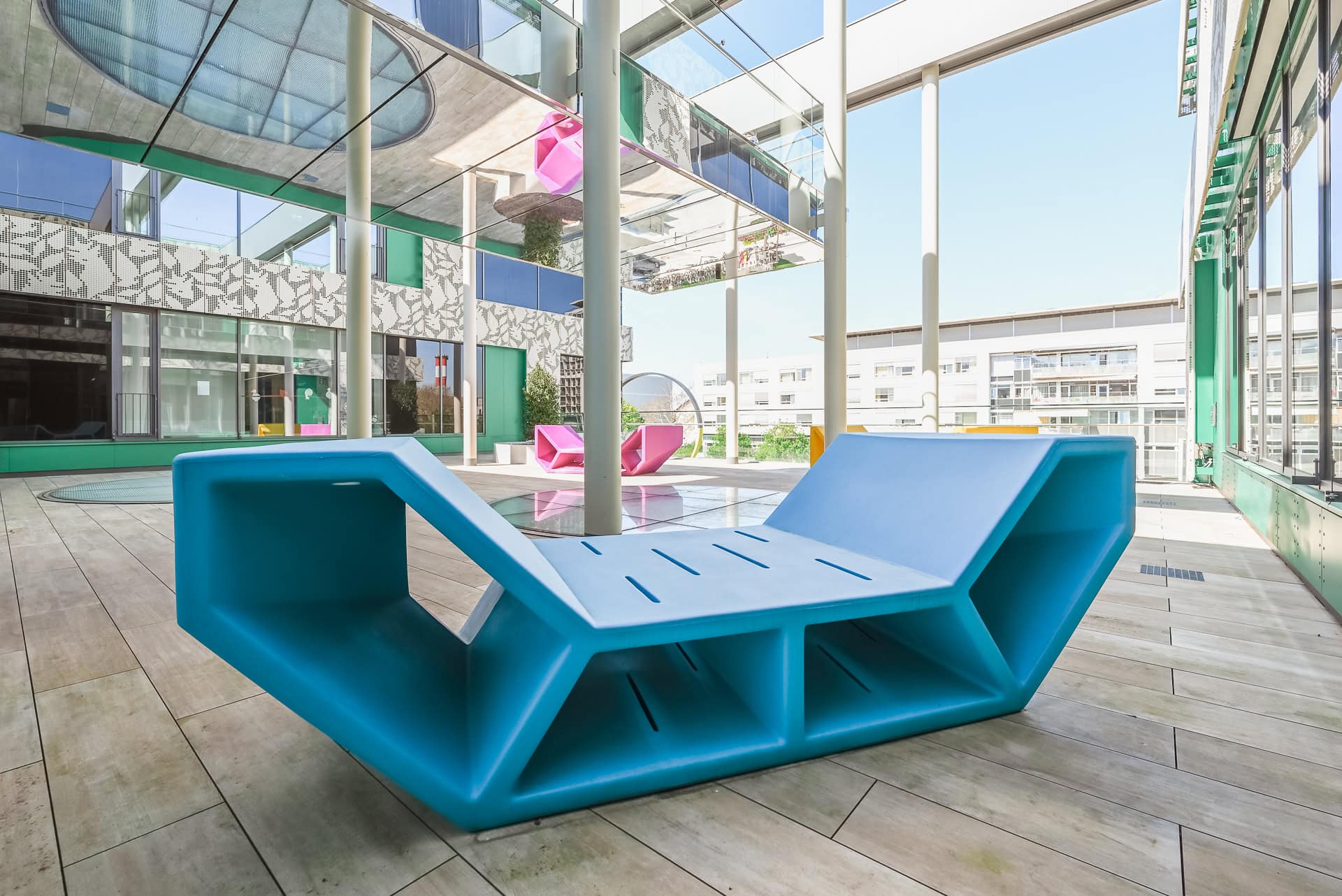 Innenhof der Kinder- und Jugendklinik Freiburg mit blauem Sitzobjekt, Spiegeldecke und farbigen Fassadenelementen. Architektur von Heinle, Wischer und Partner. Foto: Bertrand Weiss, weissfotografie.com.