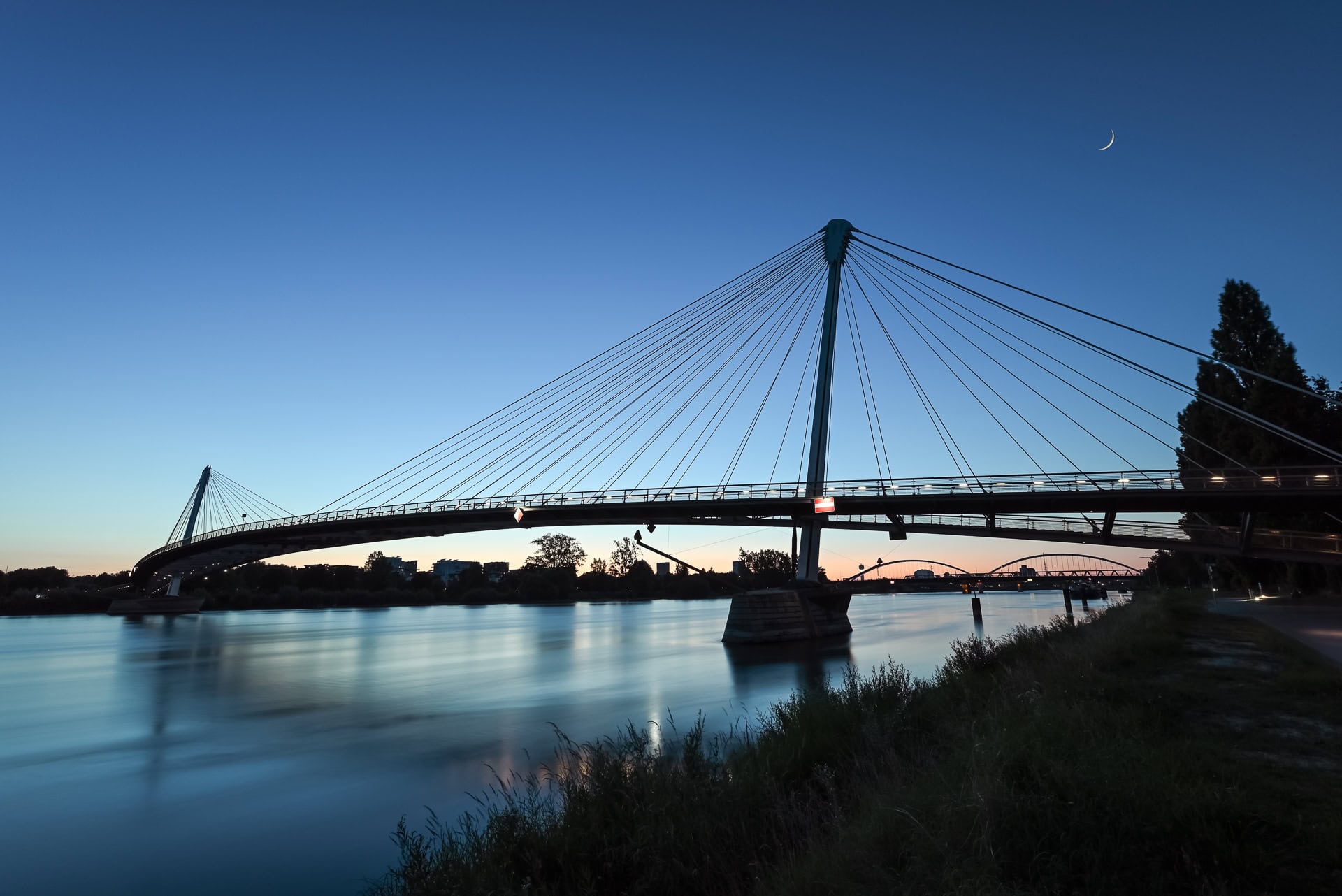 weissfotografie-kehl-strassburg-passerelle-marcmimram-06 Passerelle des Deux Rives in der Blauen Stunde mit Mondsichel über dem Rhein. Architektur von Marc Mimram Architecture & Ingénierie. Foto: Bertrand Weiss, weissfotografie.com.