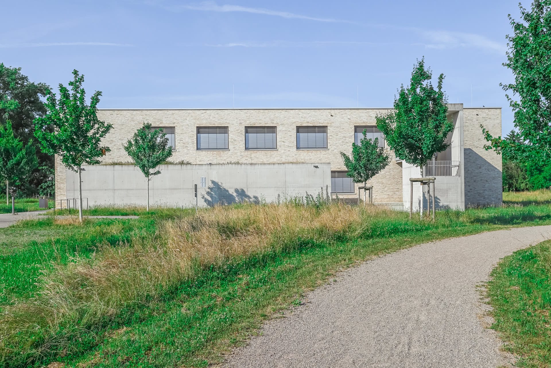 Rückseitige Ansicht des Neuen Rathauses Schallstadt mit Klinkerfassade, Betonwand und Grünraum. Architektur von OHO Architekten. Foto: Bertrand Weiss, weissfotografie.com.