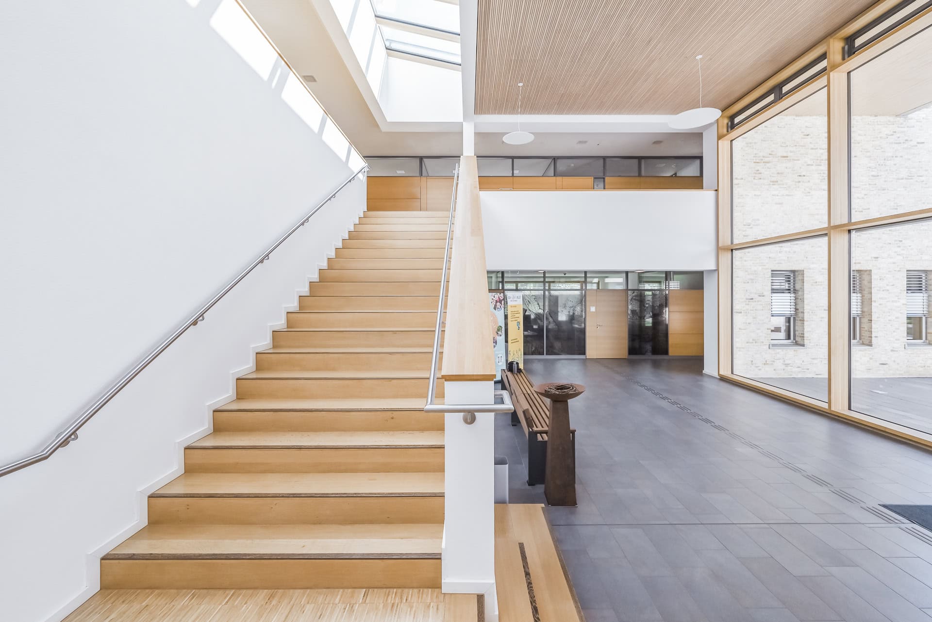 Foyer des Neuen Rathauses Schallstadt mit Holztreppe, Sitzbank und Blick zum Innenhof. Architektur von OHO Architekten. Foto: Bertrand Weiss, weissfotografie.com.