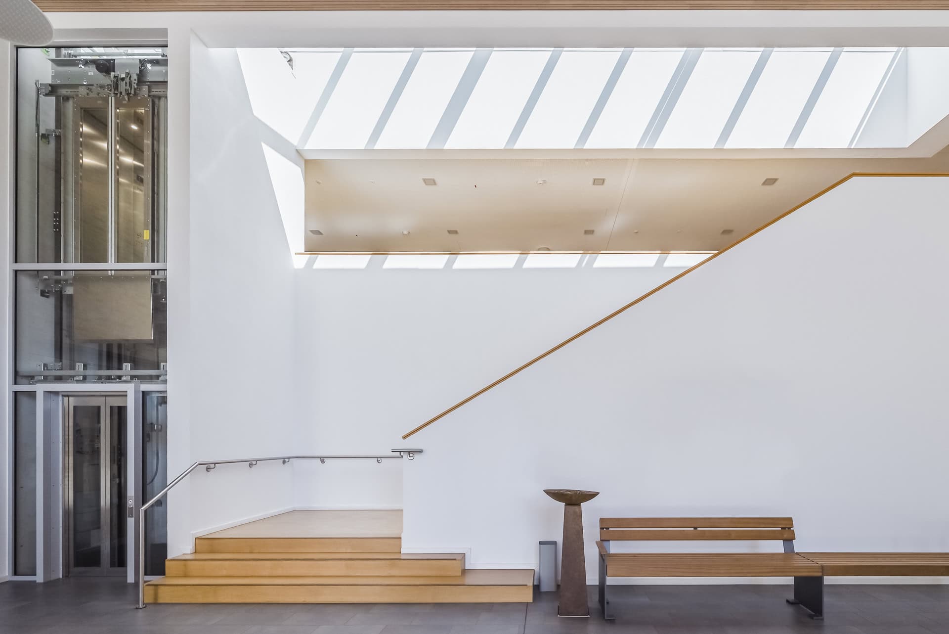 Reduzierter Innenraum des Neuen Rathauses Schallstadt mit Treppe, Aufzug und Oberlicht. Architektur von OHO Architekten. Foto: Bertrand Weiss, weissfotografie.com.