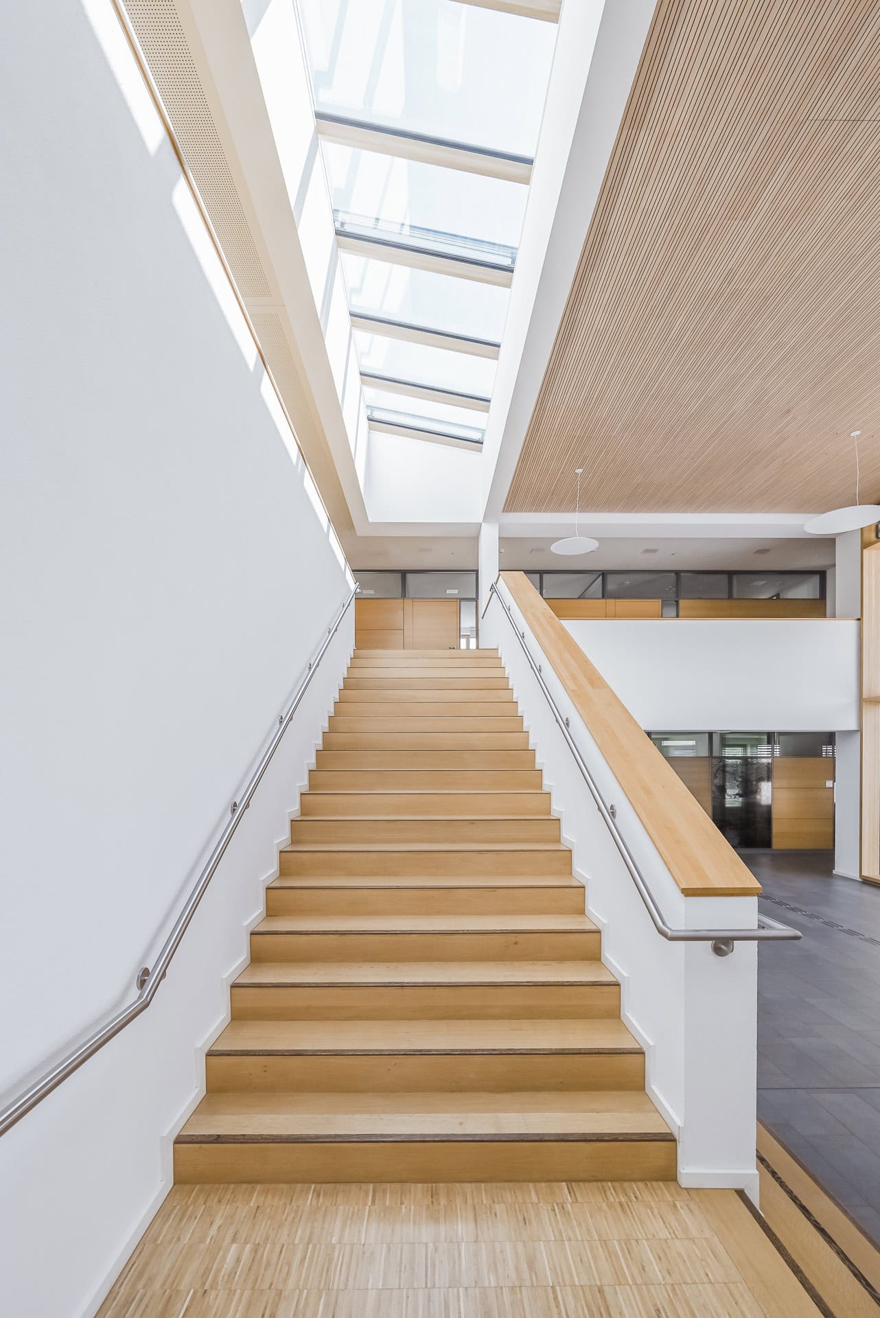 Treppenaufgang im Neuen Rathaus Schallstadt mit Holzstufen und langem Dachlicht. Architektur von OHO Architekten. Foto: Bertrand Weiss, weissfotografie.com.
