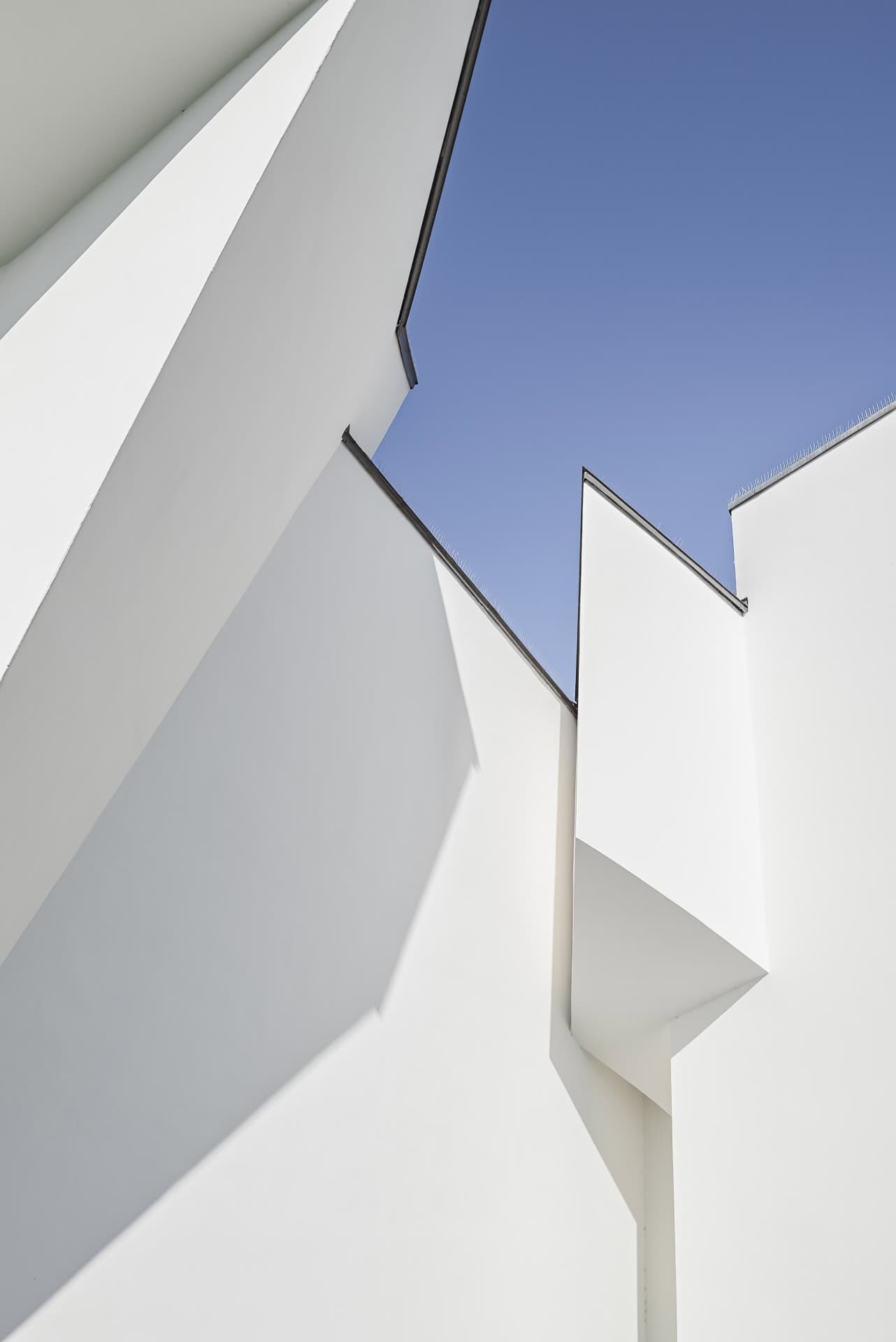 Detailaufnahme weißer Fassadenflächen des Vitra Design Museums mit scharfen Kanten und blauem Himmel. Architektur von Frank O. Gehry. Foto: Bertrand Weiss, weissfotografie.com.