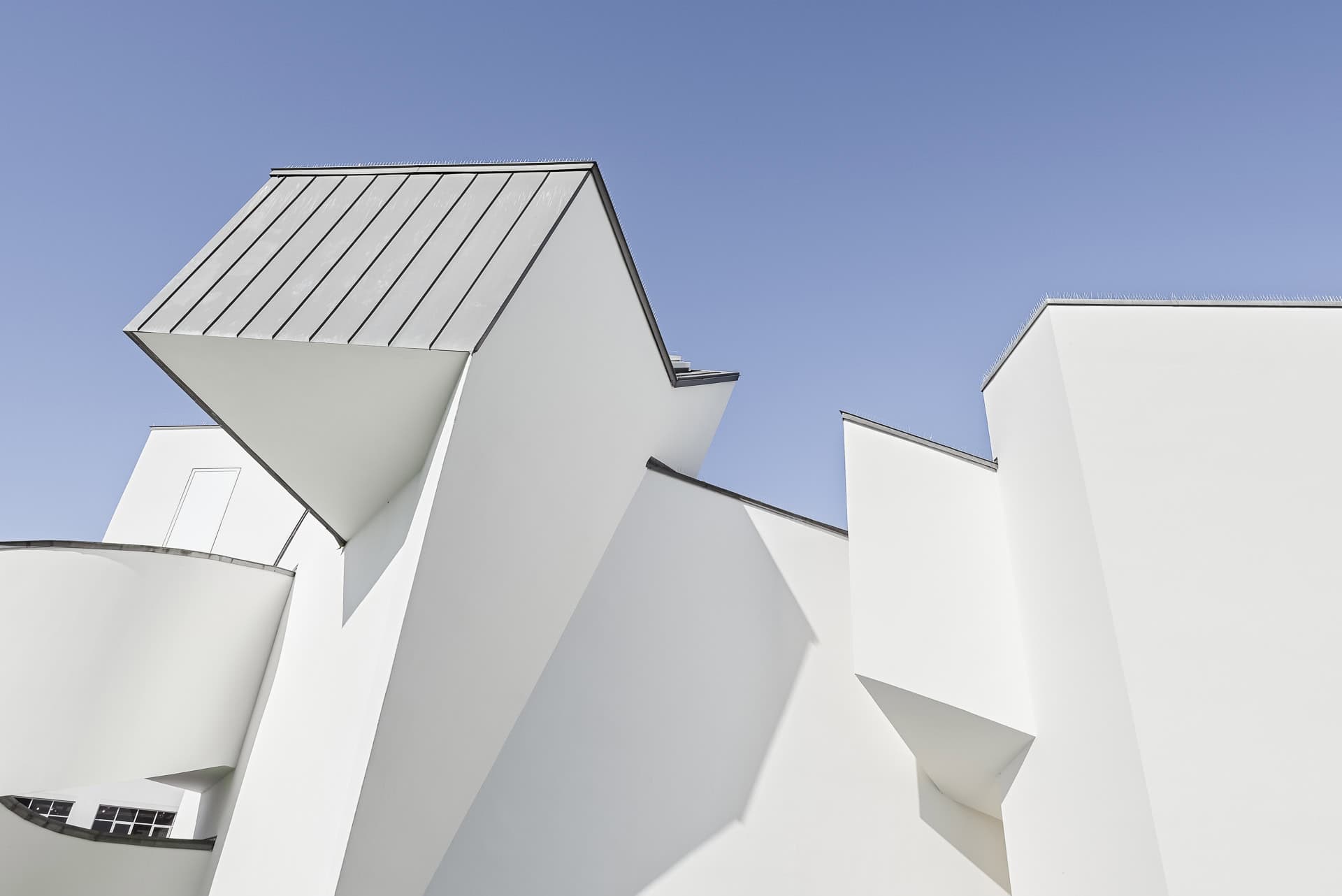 Untersicht auf die plastischen Dach- und Fassadenformen des Vitra Design Museums vor klarem Himmel. Architektur von Frank O. Gehry. Foto: Bertrand Weiss, weissfotografie.com.