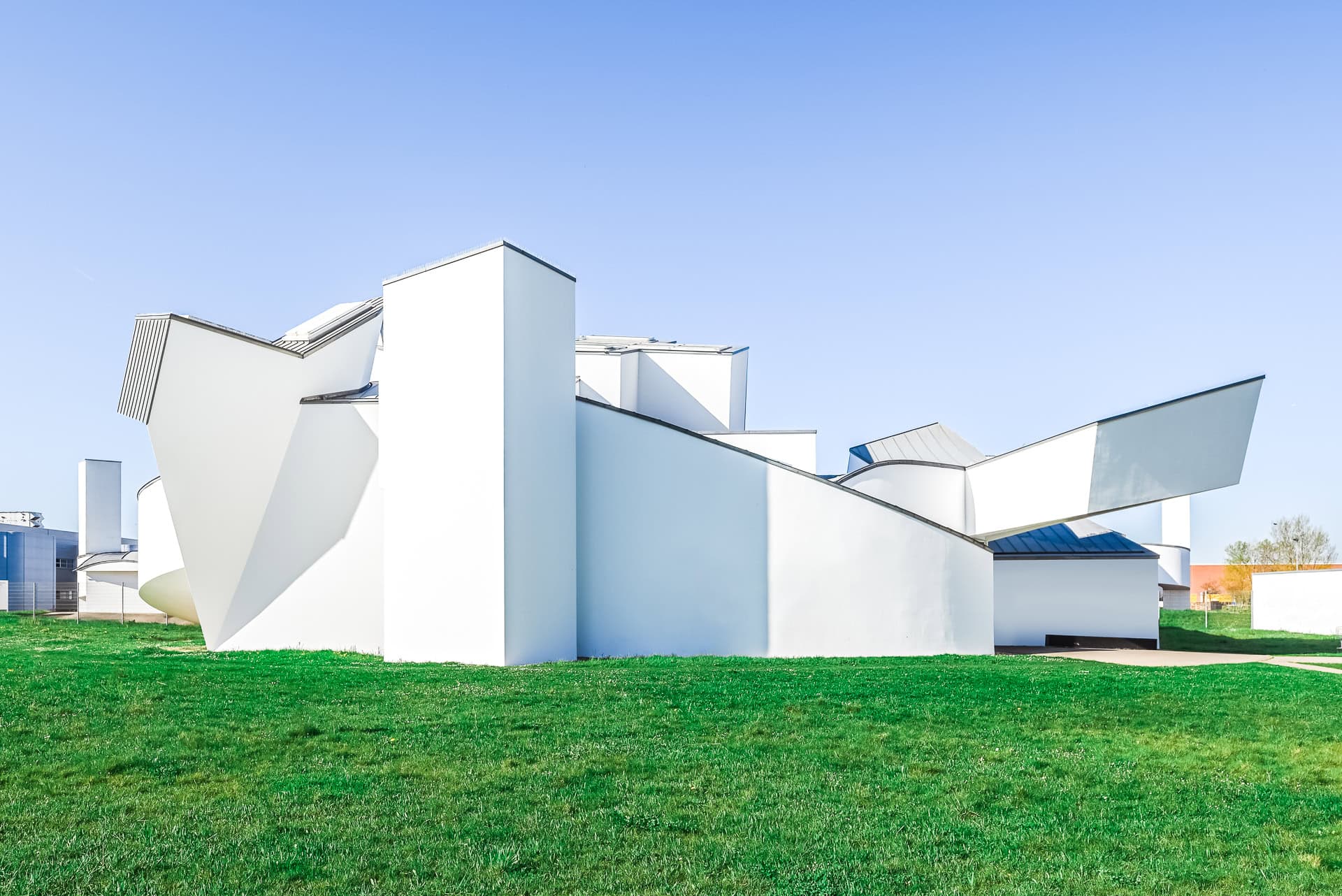 Rückseitige Außenansicht des Vitra Design Museums mit gestaffelten weißen Baukörpern im Grünraum. Architektur von Frank O. Gehry. Foto: Bertrand Weiss, weissfotografie.com.