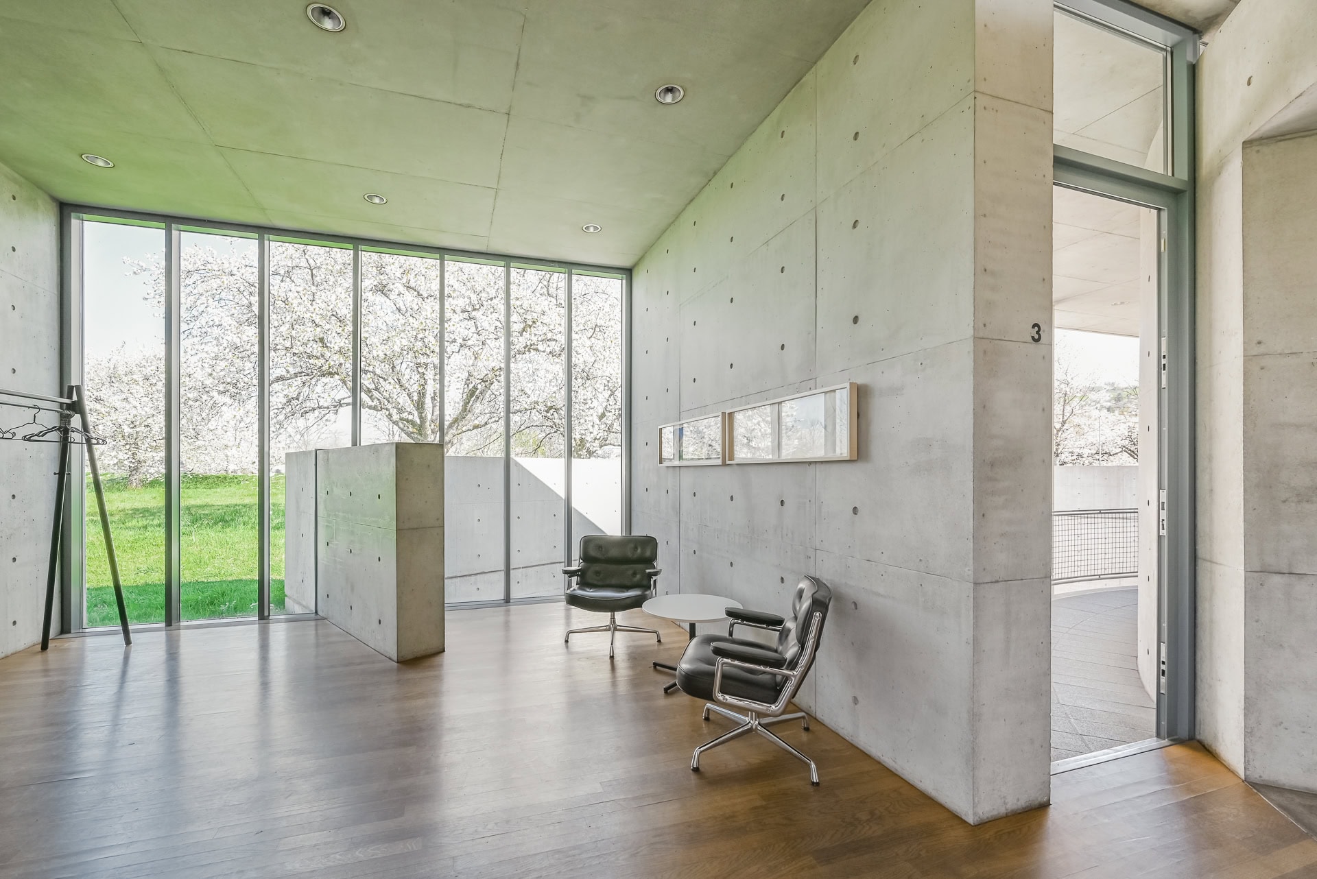 Innenraum des Vitra Konferenzpavillons mit Sichtbeton, Holzfußboden und großem Fenster zum Grünraum. Architektur von Tadao Ando. Foto: Bertrand Weiss, weissfotografie.com.