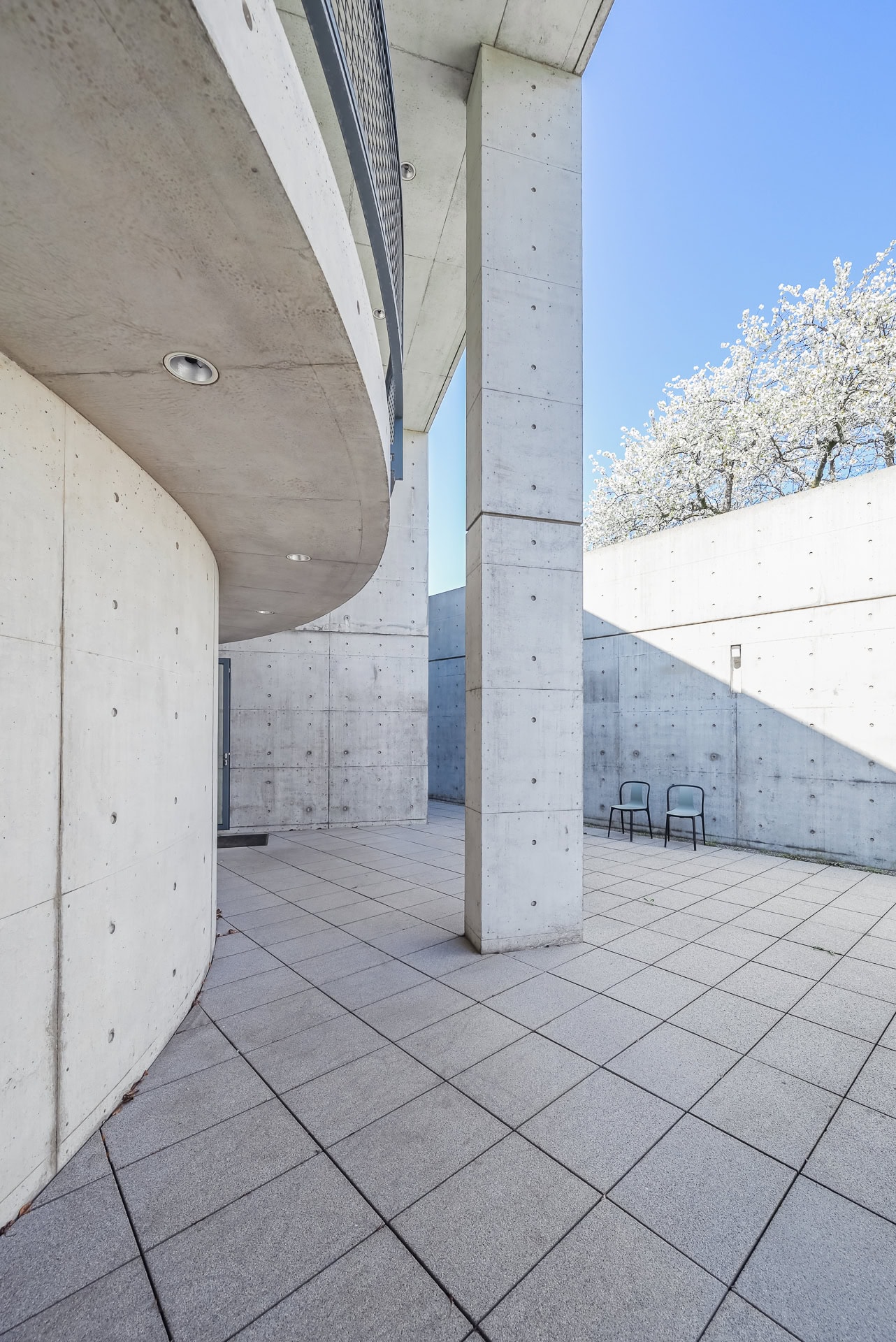 Außenhof des Vitra Konferenzpavillons mit Sichtbetonwänden, Stützen und zwei Stühlen im Licht. Architektur von Tadao Ando. Foto: Bertrand Weiss, weissfotografie.com.