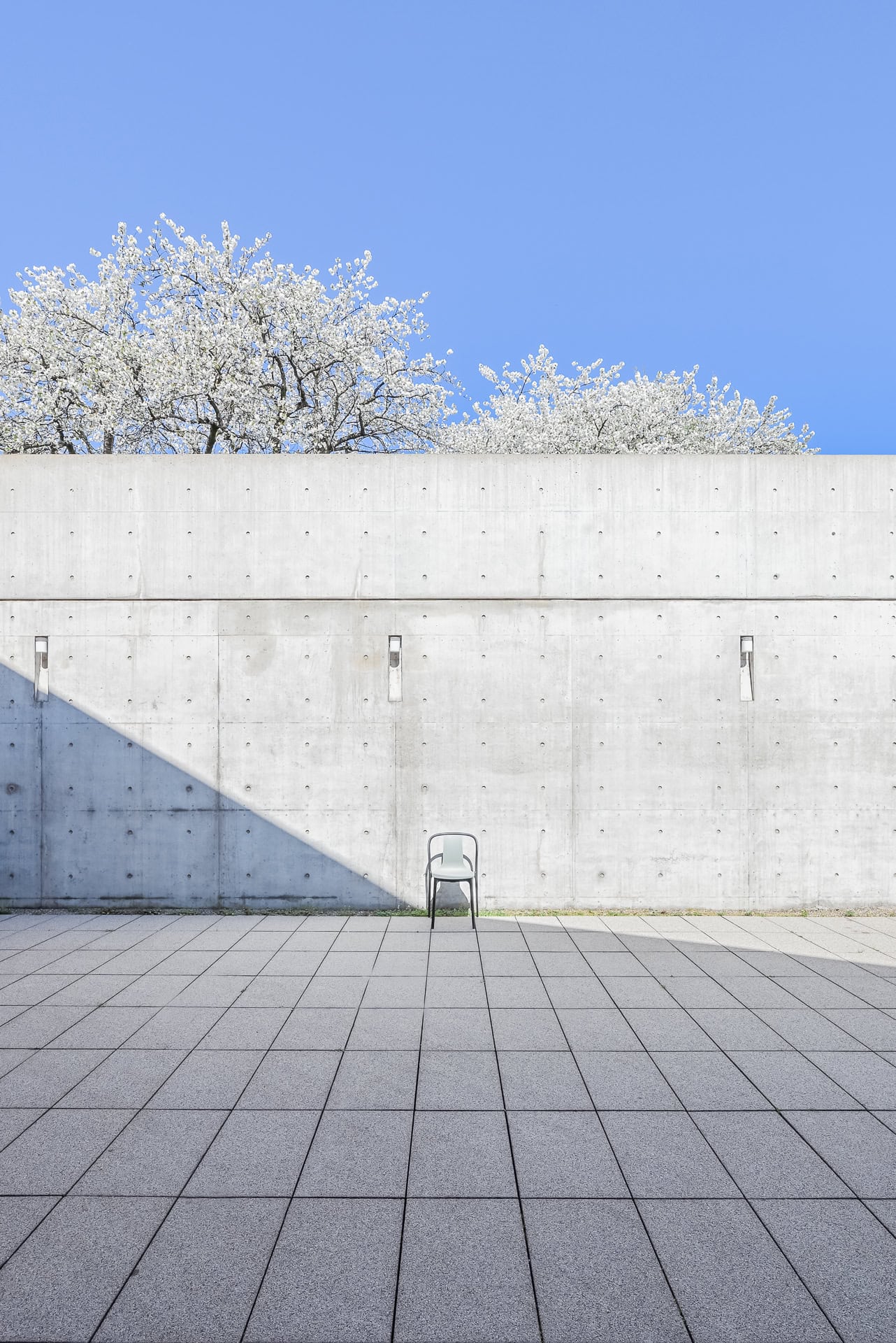 Reduzierter Hofraum des Vitra Konferenzpavillons mit Betonwand, Stuhl und blühenden Bäumen. Architektur von Tadao Ando. Foto: Bertrand Weiss, weissfotografie.com.