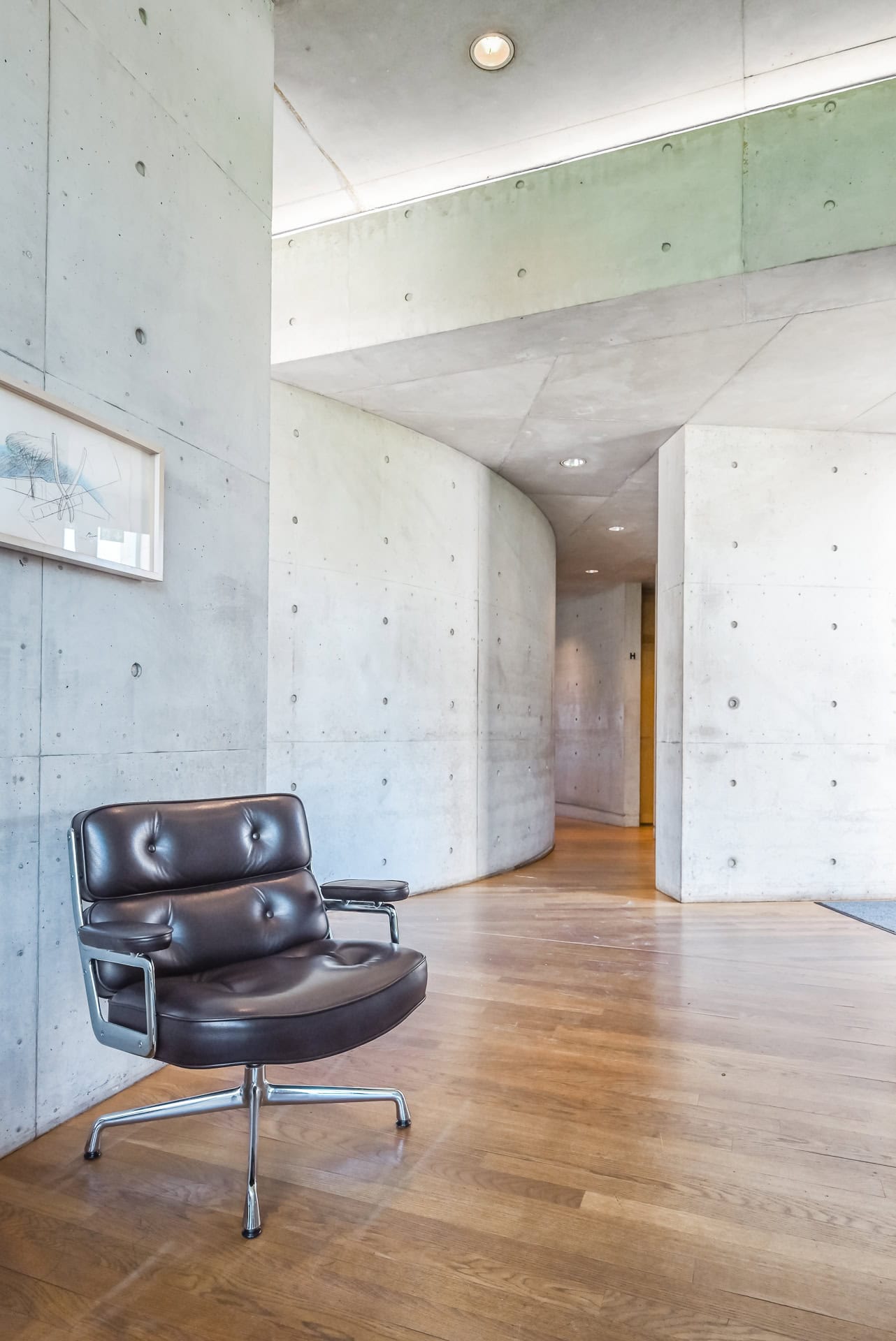 Innenraum des Vitra Konferenzpavillons mit Ledersessel, gebogener Betonwand und Holzfußboden. Architektur von Tadao Ando. Foto: Bertrand Weiss, weissfotografie.com.