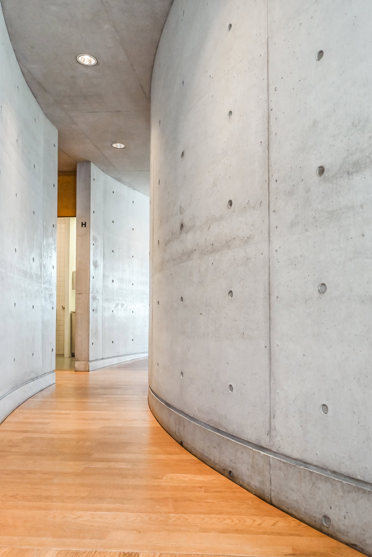 Geschwungener Gang im Vitra Konferenzpavillon mit Sichtbetonwänden und warmem Holzfußboden. Architektur von Tadao Ando. Foto: Bertrand Weiss, weissfotografie.com.