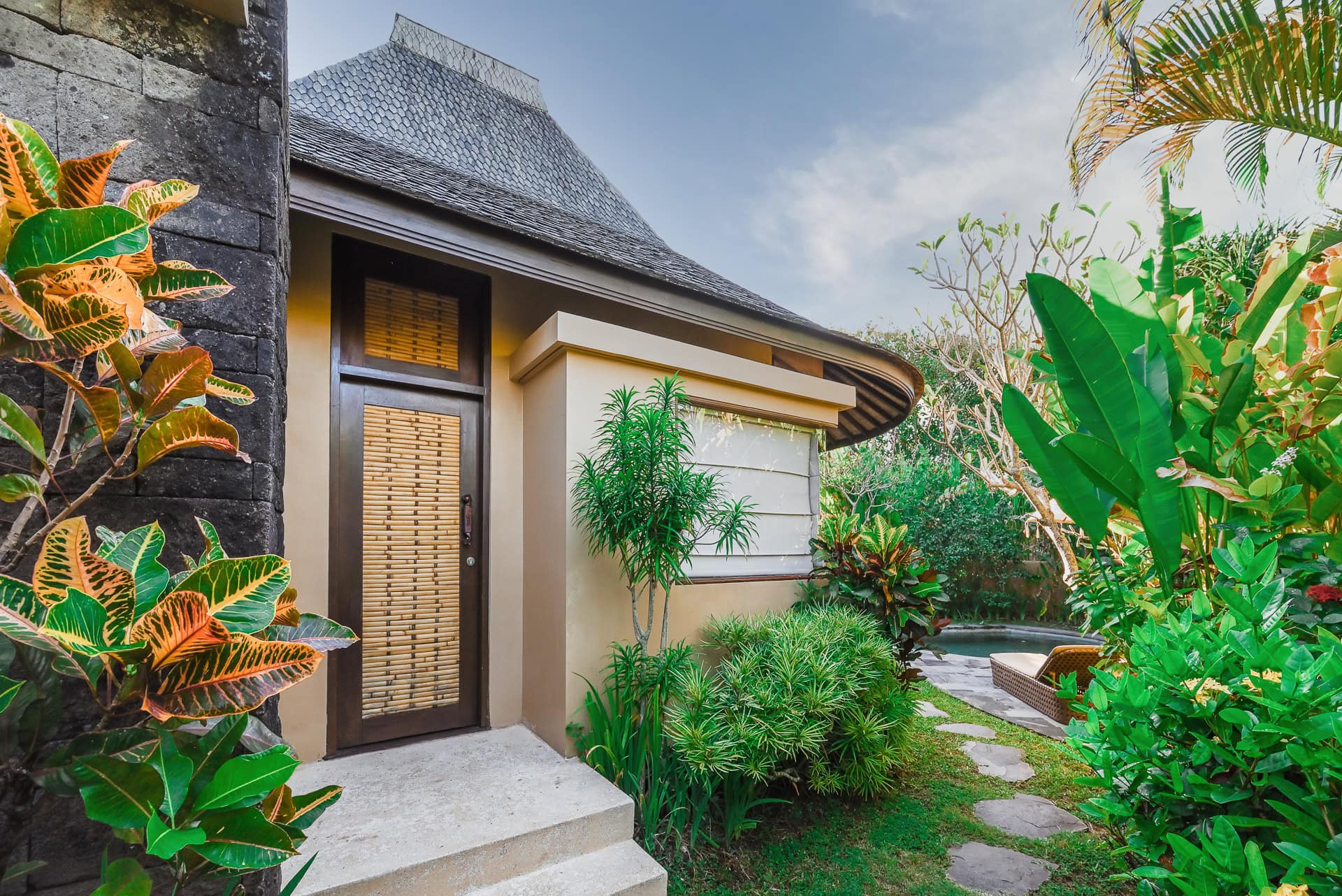 Eingangsbereich einer Villa mit Naturstein, Holz und dichter tropischer Bepflanzung. Architektur von I Ketut Siandana. Foto: Bertrand Weiss, weissfotografie.com.