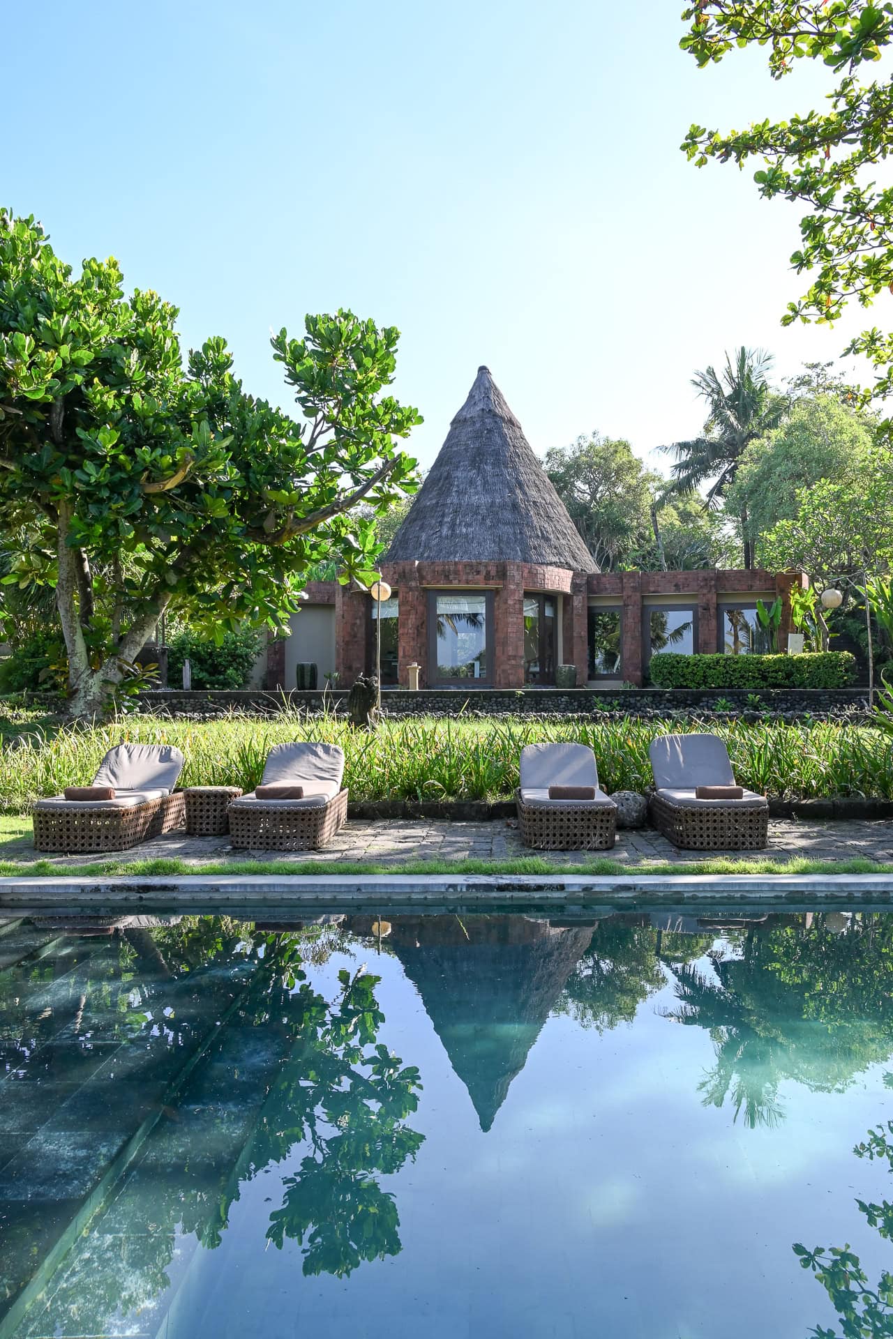 Pool und Gartenanlage mit Palmen und Blick auf das Meer in der Abenddämmerung. Architektur von I Ketut Siandana. Foto: Bertrand Weiss, weissfotografie.com.