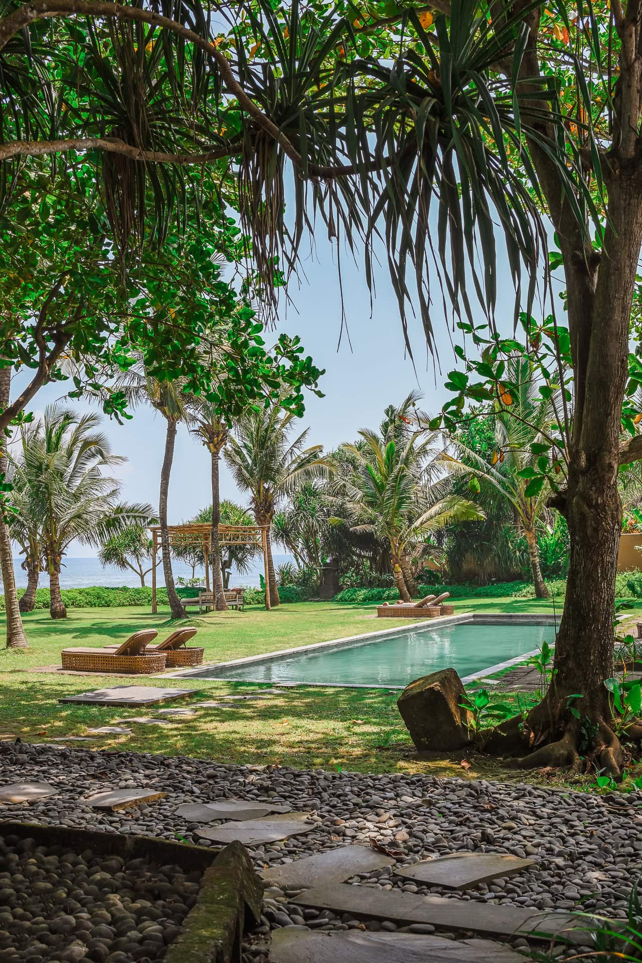 Tropischer Garten mit Pool, Liegen und dichtem Baumbestand nahe der Küste. Architektur von I Ketut Siandana. Foto: Bertrand Weiss, weissfotografie.com.