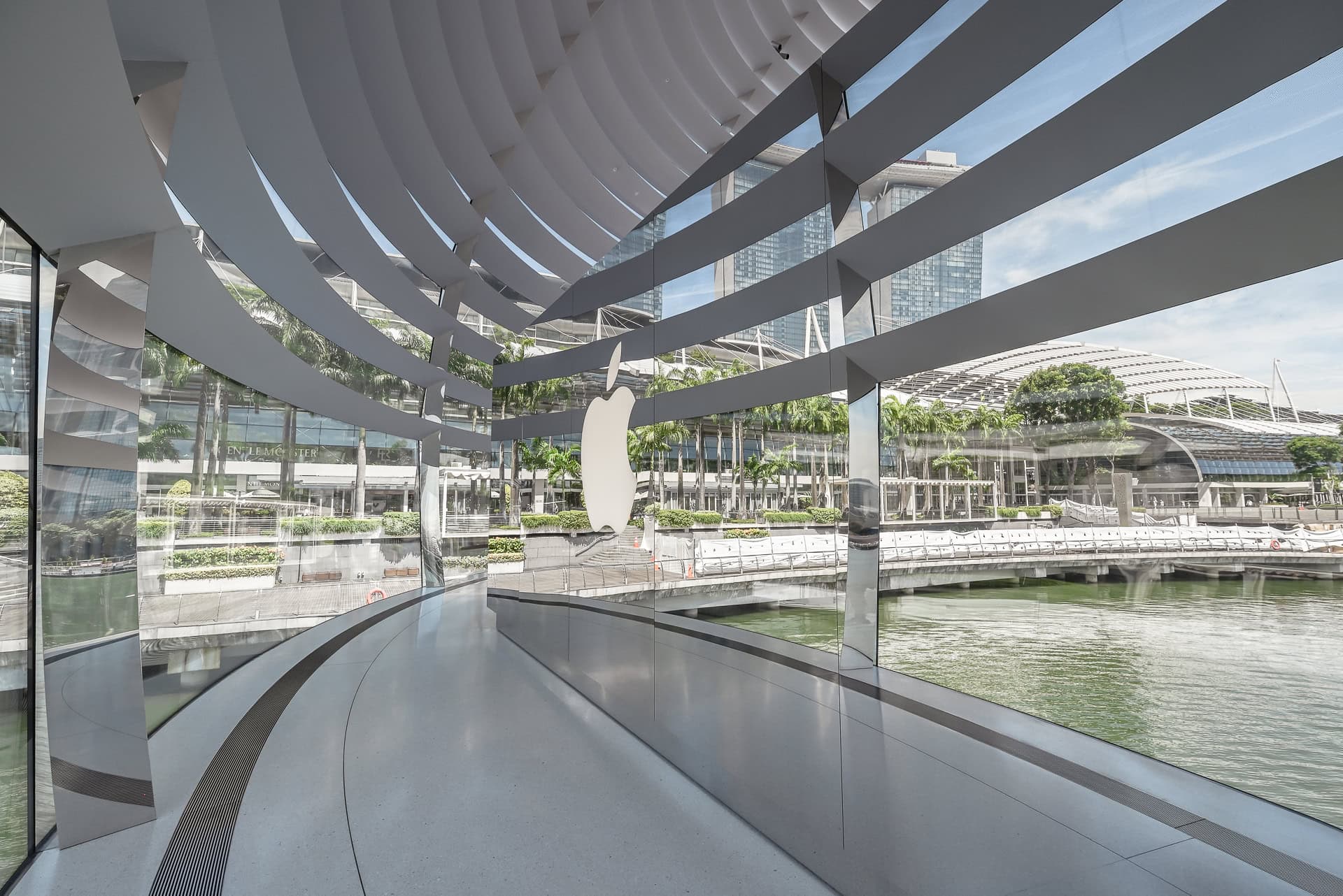 Blick durch die gebogenen Glasflächen des Apple Store auf Marina Bay Sands und die Uferpromenade. Architektur von Foster + Partners. Foto: Bertrand Weiss, weissfotografie.com.