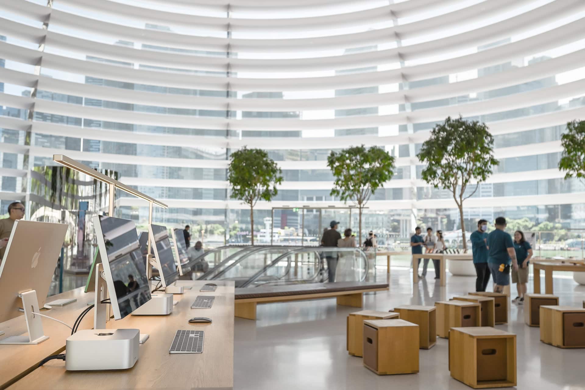 Heller Innenraum des Apple Marina Bay Sands mit Produktmöbeln, Bäumen und horizontalen Sonnenschutzlamellen. Architektur von Foster + Partners. Foto: Bertrand Weiss, weissfotografie.com.