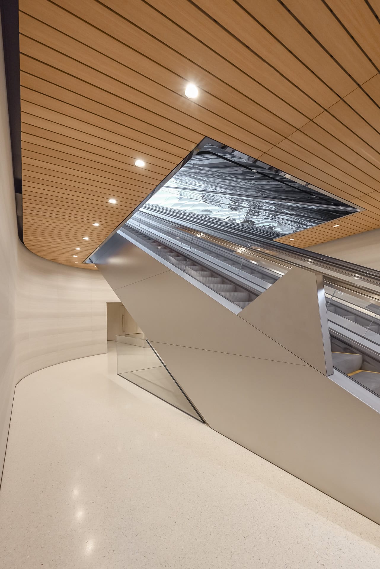 Untergeschoss des Apple Store mit Rolltreppe, heller Wandgestaltung und Holzdecke. Architektur von Foster + Partners. Foto: Bertrand Weiss, weissfotografie.com.