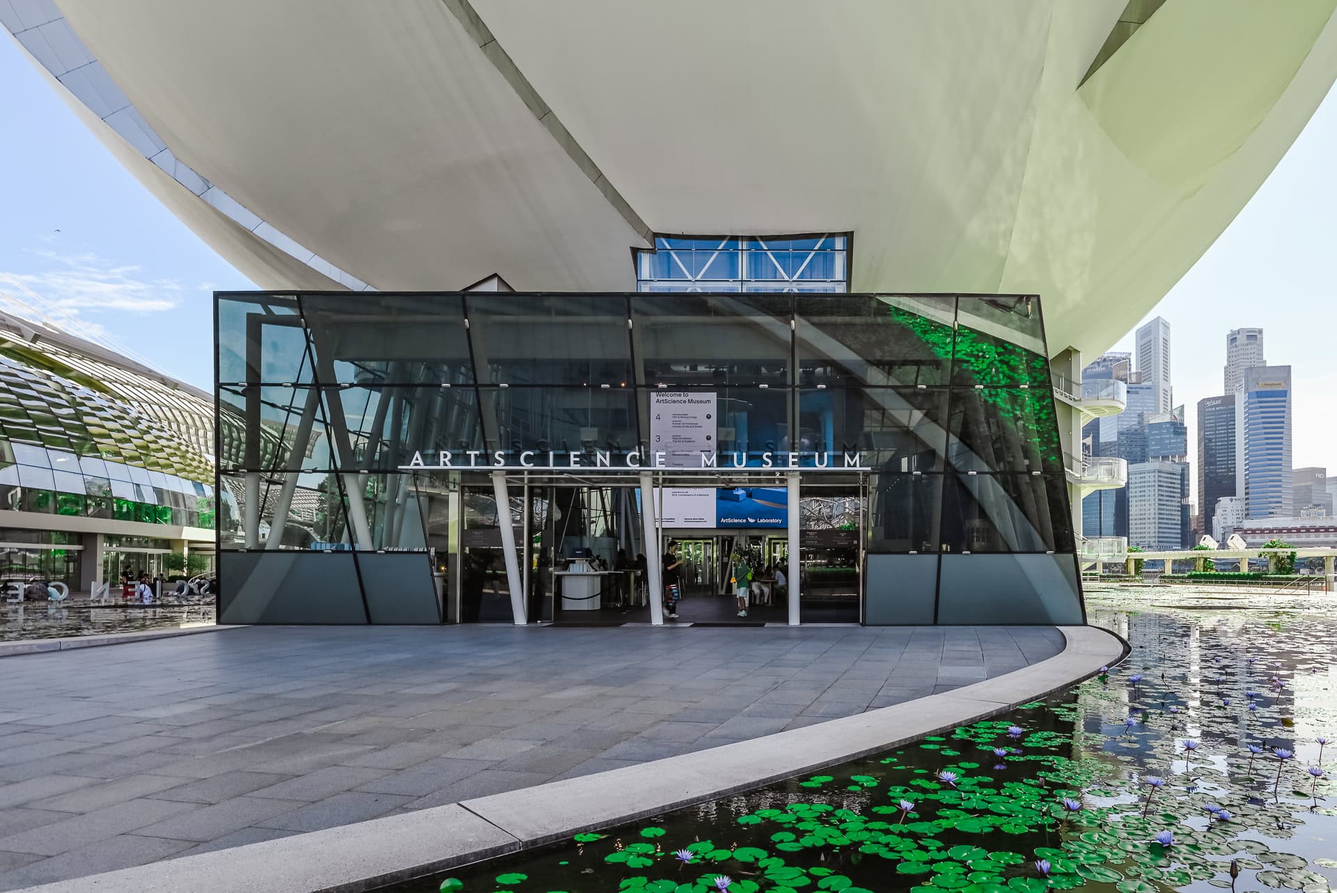 Eingangsbereich des ArtScience Museum unter den auskragenden weißen Baukörpern mit Wasserbecken und Seerosen. Architektur von Safdie Architects. Foto: Bertrand Weiss, weissfotografie.com.