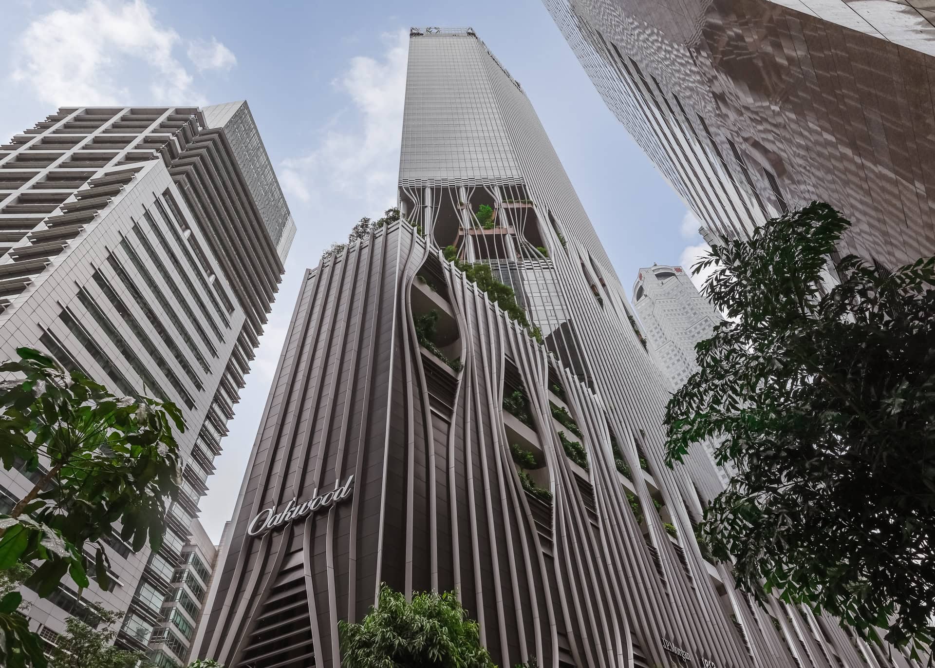 CapitaSpring aus der Froschperspektive zwischen den umliegenden Hochhäusern mit begrünten Öffnungen in der Fassade. Architektur von BIG und CRA. Foto: Bertrand Weiss, weissfotografie.com.