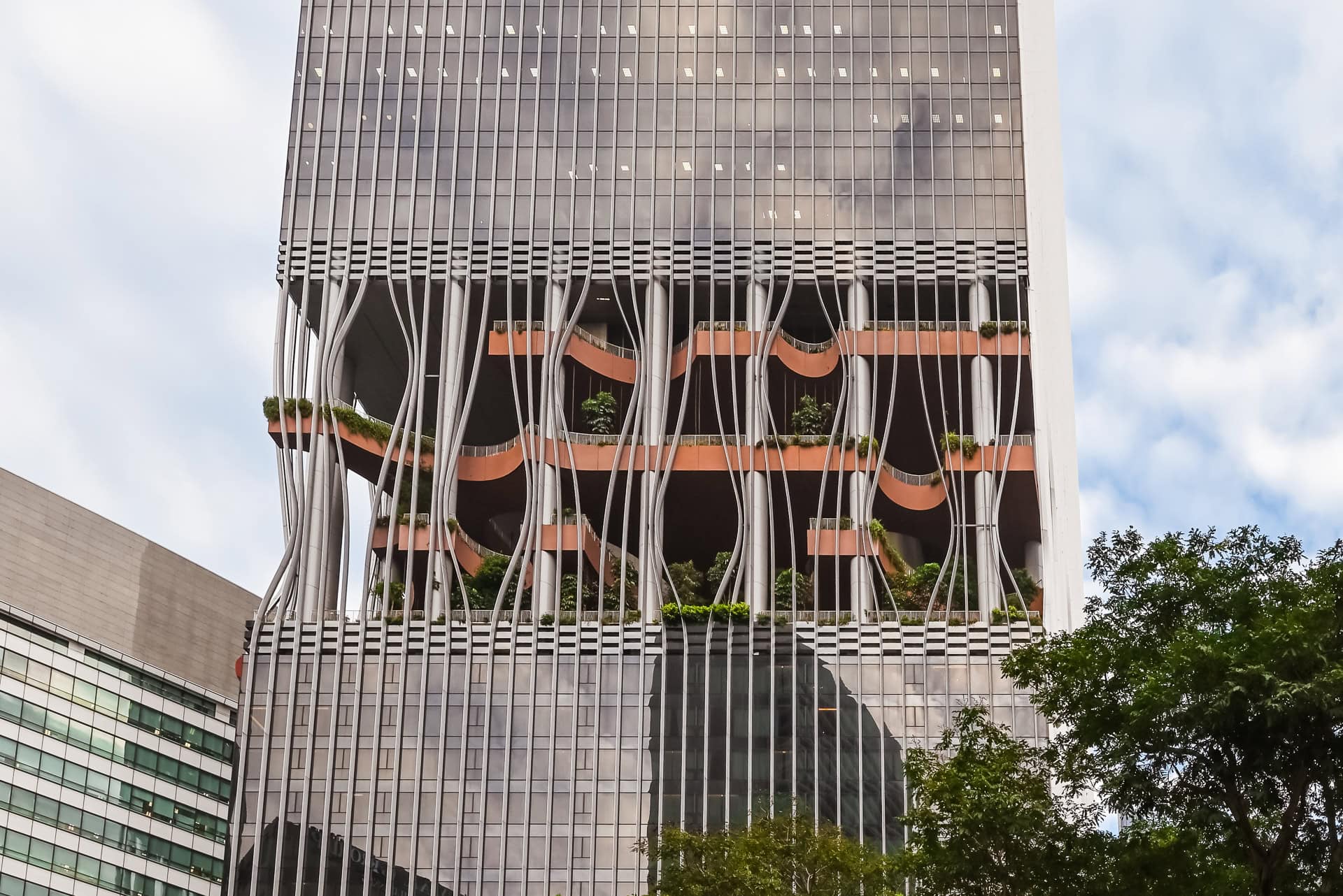 Steil aufragende Fassade des CapitaSpring mit geöffneten begrünten Bereichen und vertikaler Metallstruktur. Architektur von BIG und CRA. Foto: Bertrand Weiss, weissfotografie.com.