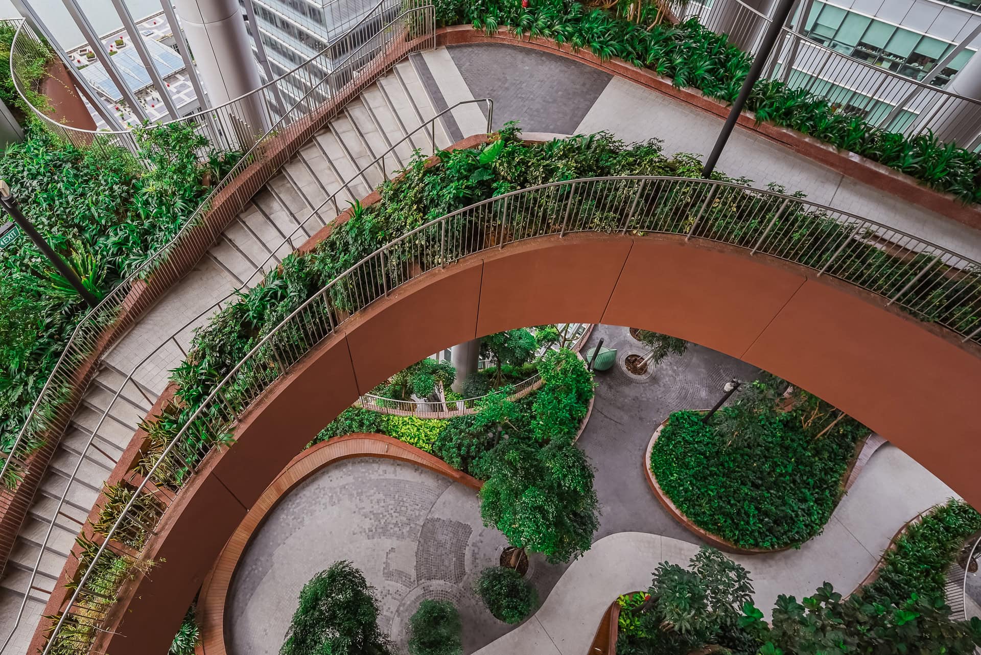 Geschwungene Wege und Terrassen der begrünten Zwischenzone mit Bäumen und dichter Vegetation. Architektur von BIG und CRA. Foto: Bertrand Weiss, weissfotografie.com.