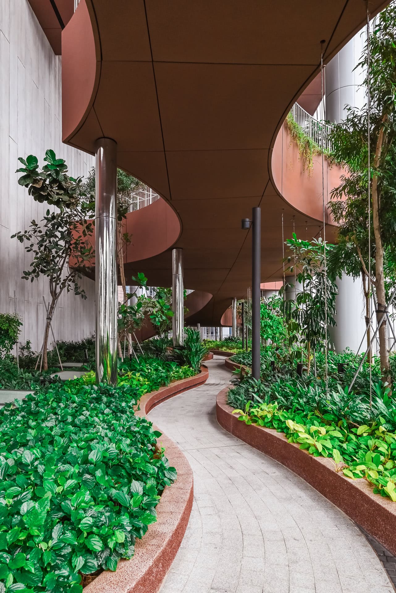 Überdachter Gartenweg zwischen geschwungenen Terrassen, Metallstützen und tropischer Bepflanzung. Architektur von BIG und CRA. Foto: Bertrand Weiss, weissfotografie.com.