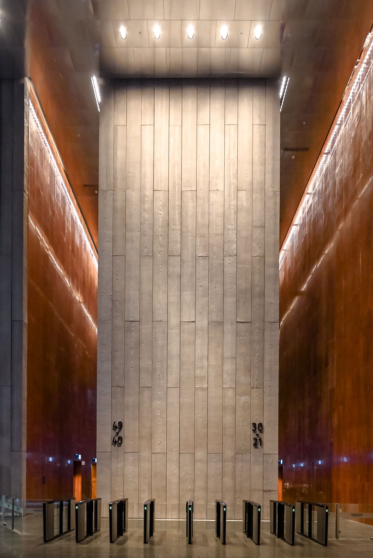 Hohe Lobby mit warmen Wandflächen, heller Steinwand und symmetrisch angeordneten Zugangsschleusen. Architektur von BIG und CRA. Foto: Bertrand Weiss, weissfotografie.com.