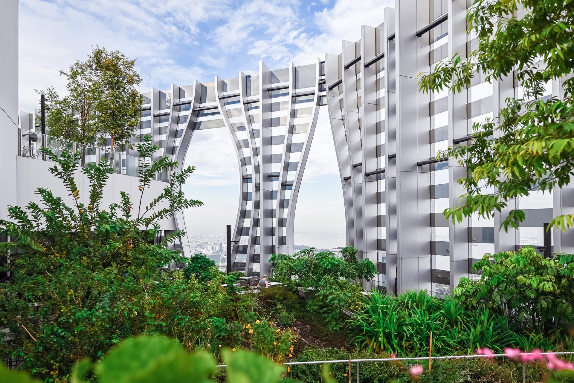 Gartenebene mit silbernen Fassadenlamellen, üppiger Vegetation und weitem Blick über die Stadt. Architektur von BIG und CRA. Foto: Bertrand Weiss, weissfotografie.com.