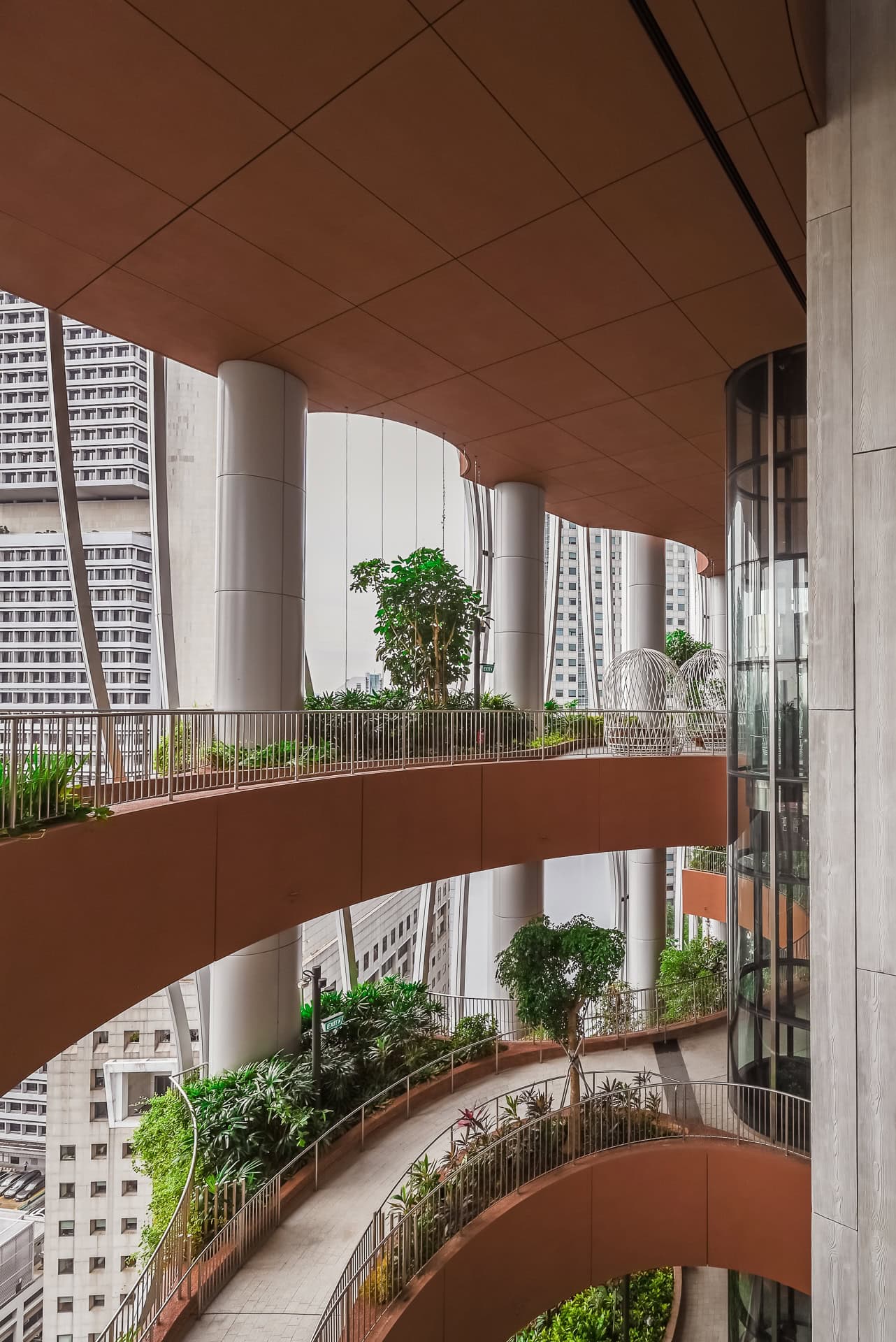 Geschwungene Wege und Terrassen der begrünten Zwischenzone mit Bäumen und dichter Vegetation. Architektur von BIG und CRA. Foto: Bertrand Weiss, weissfotografie.com.