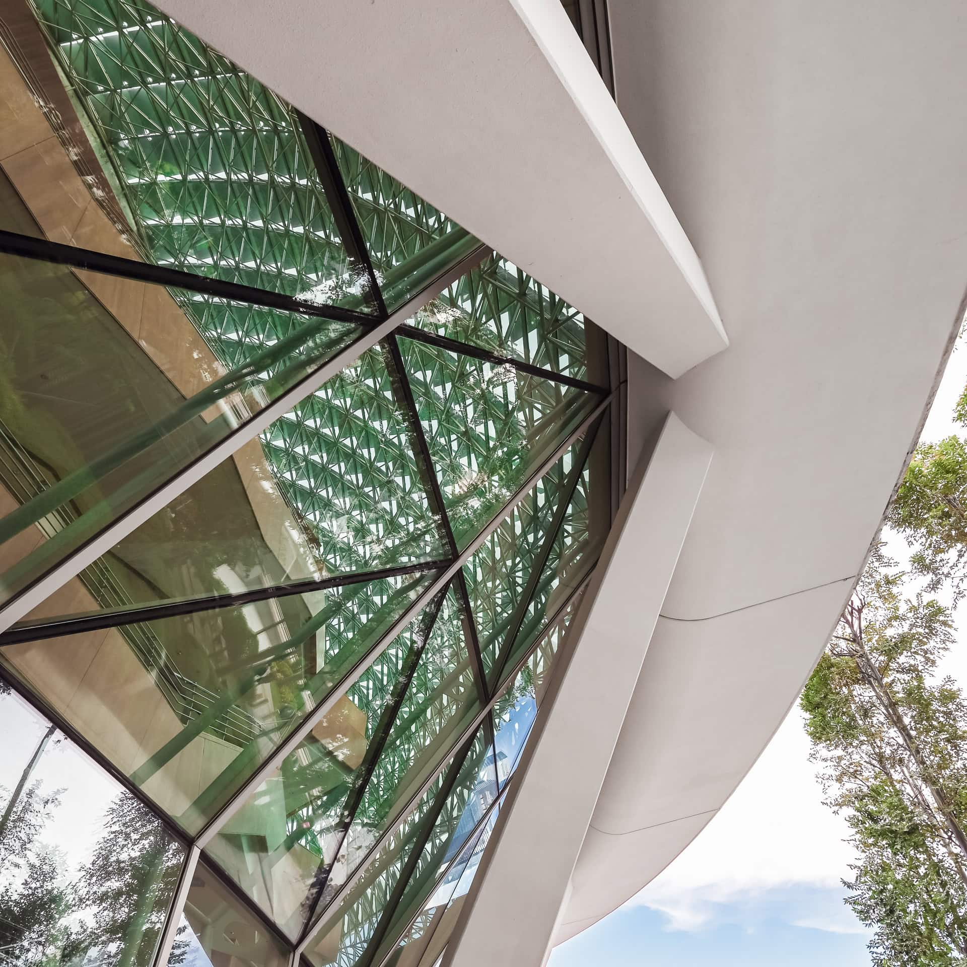 Detailansicht der dreidimensionalen Fassadenhülle mit Sonnenschutzlamellen, Glas und begrüntem Vorbereich. Architektur von DP Architects und Michael Wilford & Partners. Foto: Bertrand Weiss, weissfotografie.com.