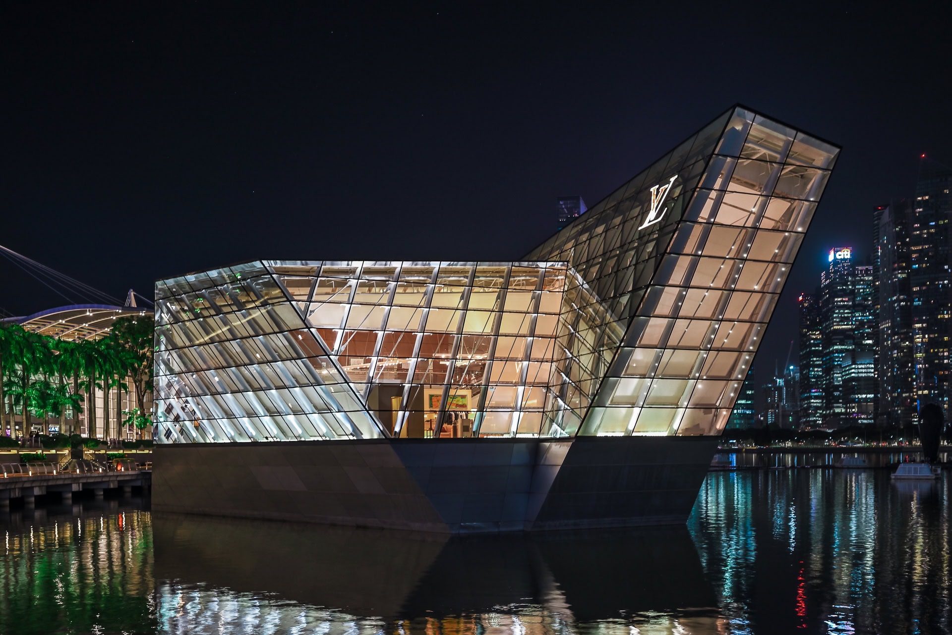 Louis Vuitton Island Maison bei Nacht mit leuchtender Glasfassade und Spiegelungen im Wasser. Architektur von Safdie Architects. Foto: Bertrand Weiss, weissfotografie.com.