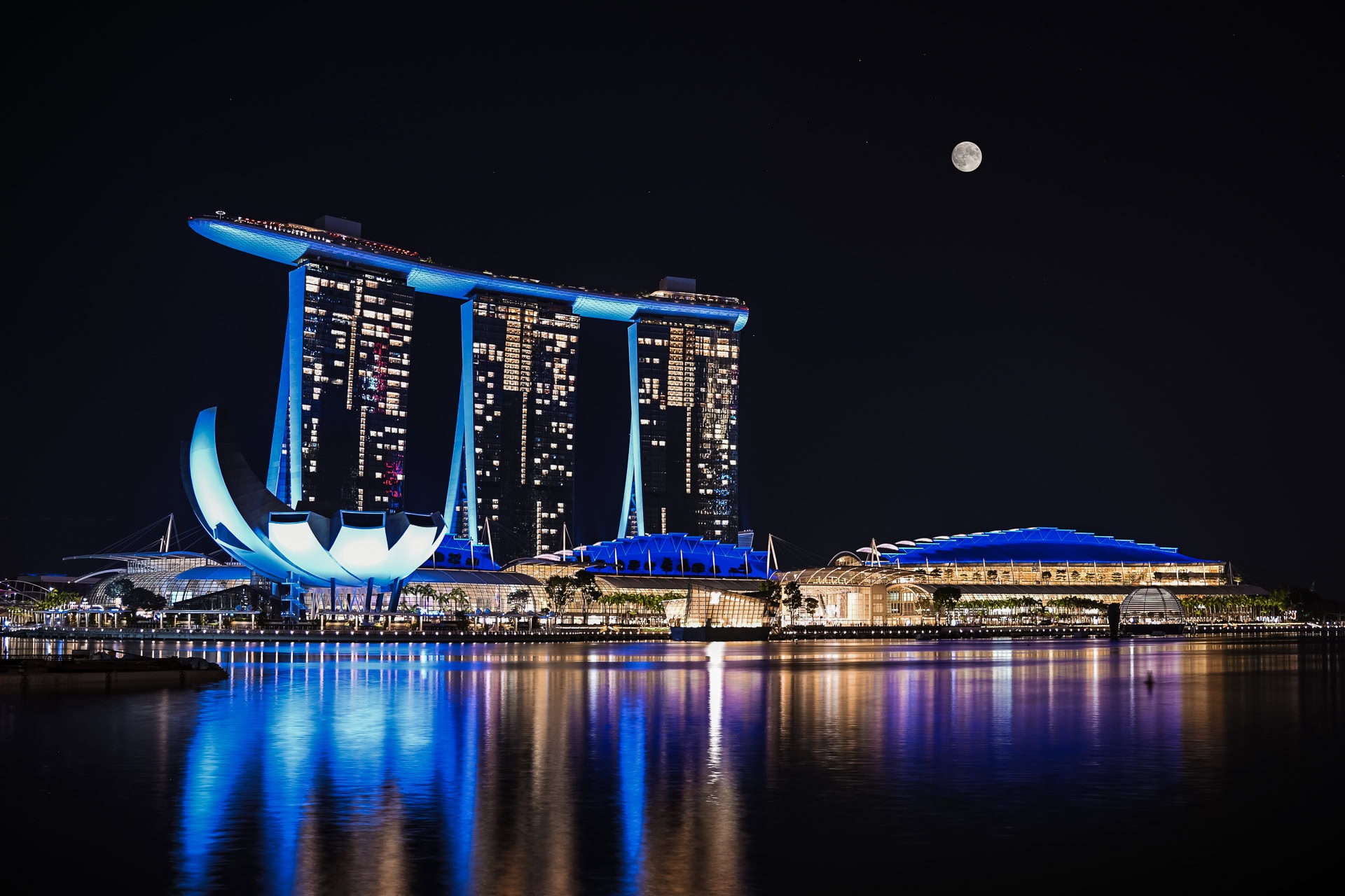 Marina Bay Sands bei Nacht mit beleuchteten Hoteltürmen, SkyPark und Spiegelungen im Wasser. Architektur von Safdie Architects. Foto: Bertrand Weiss, weissfotografie.com.