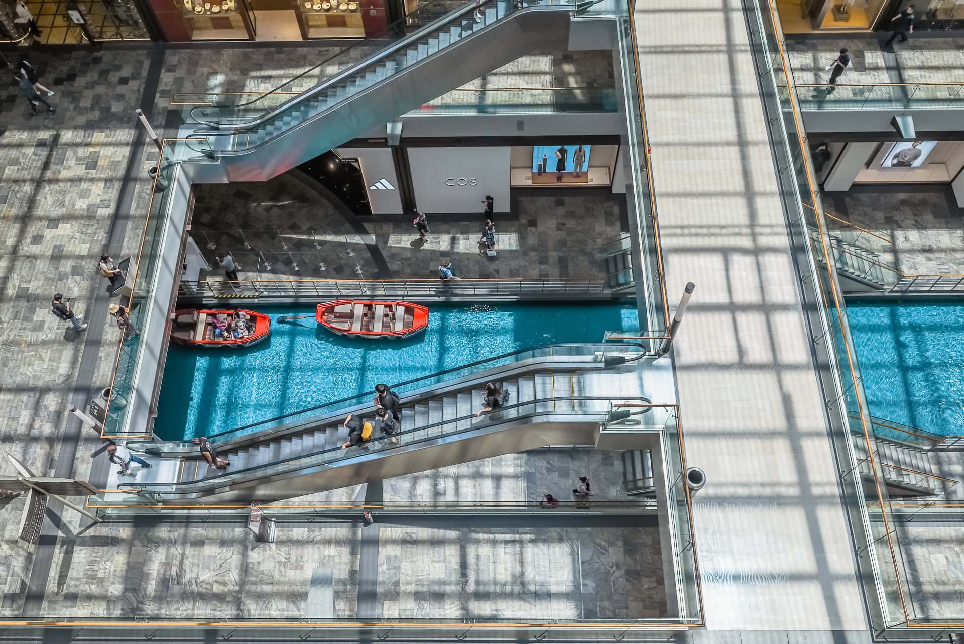 Blick von oben auf Rolltreppen, Wasserbecken und die Wege im Inneren der Shoppingpassage. Architektur von Safdie Architects. Foto: Bertrand Weiss, weissfotografie.com.