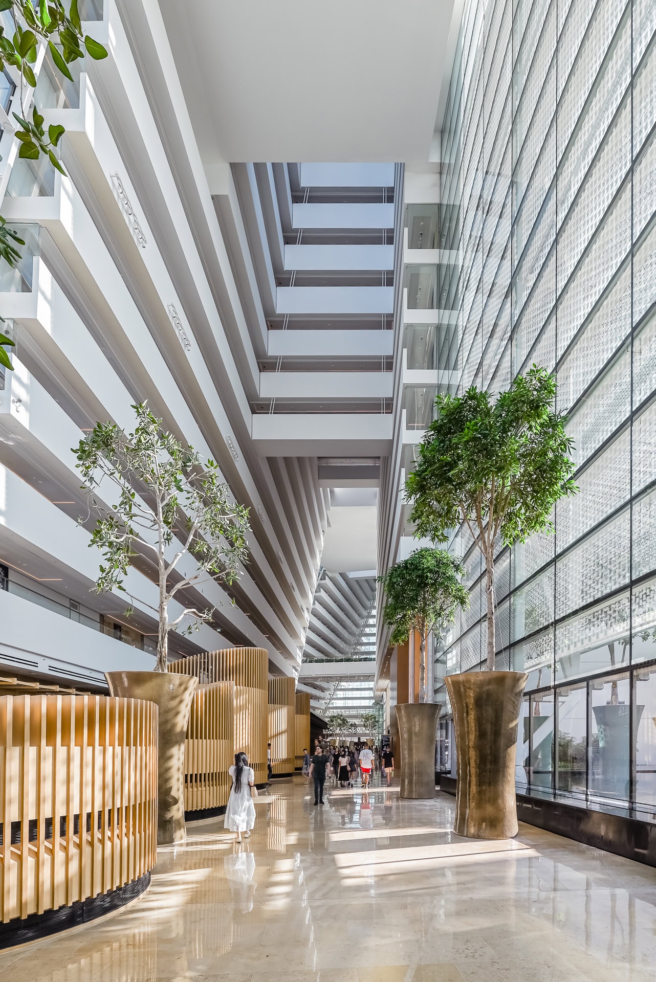 Helle Innenpassage mit mehrgeschossigen Galerien, Bäumen und großen Glasflächen. Architektur von Safdie Architects. Foto: Bertrand Weiss, weissfotografie.com.