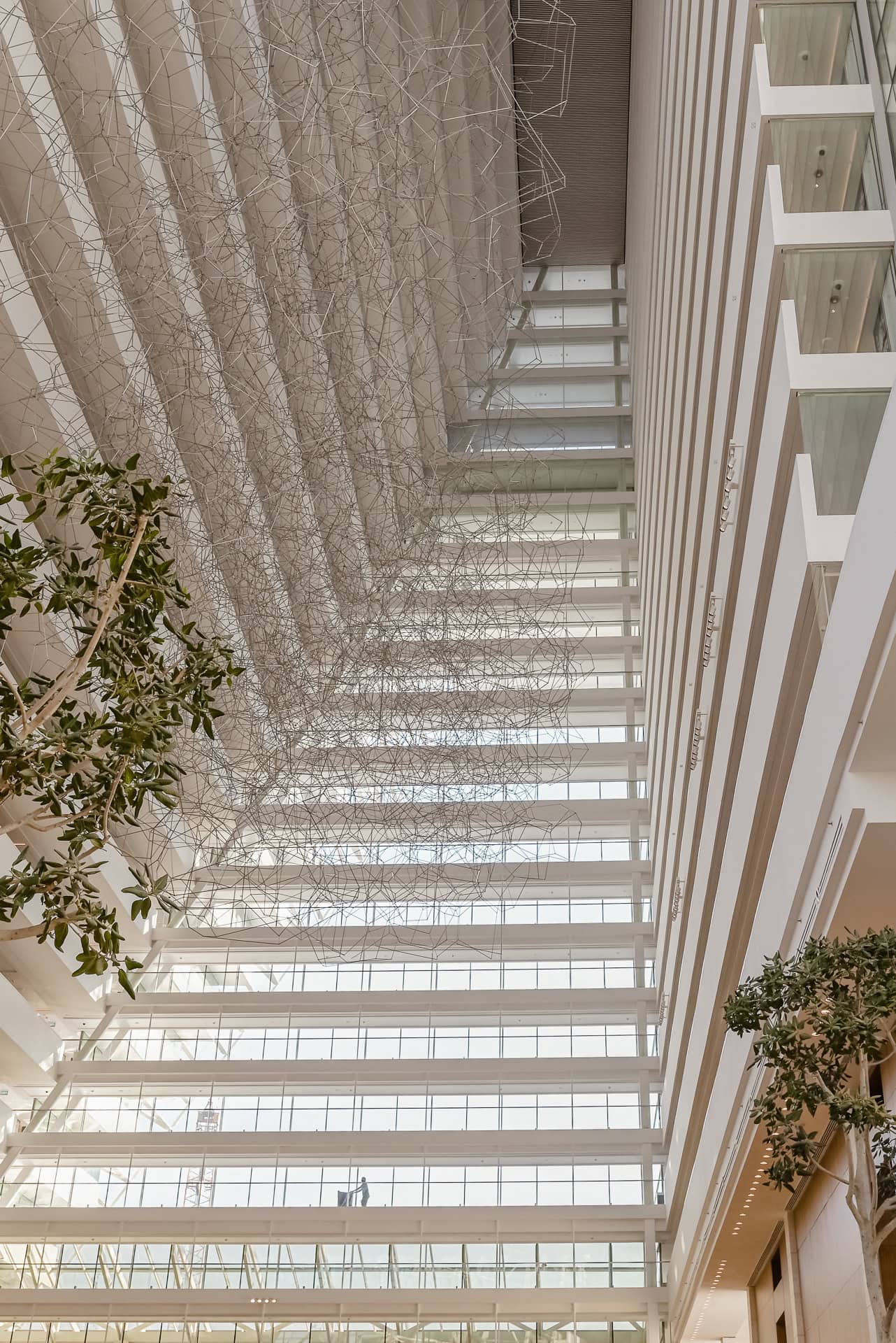 Helle Innenpassage mit mehrgeschossigen Galerien, Bäumen und großen Glasflächen. Architektur von Safdie Architects. Foto: Bertrand Weiss, weissfotografie.com.